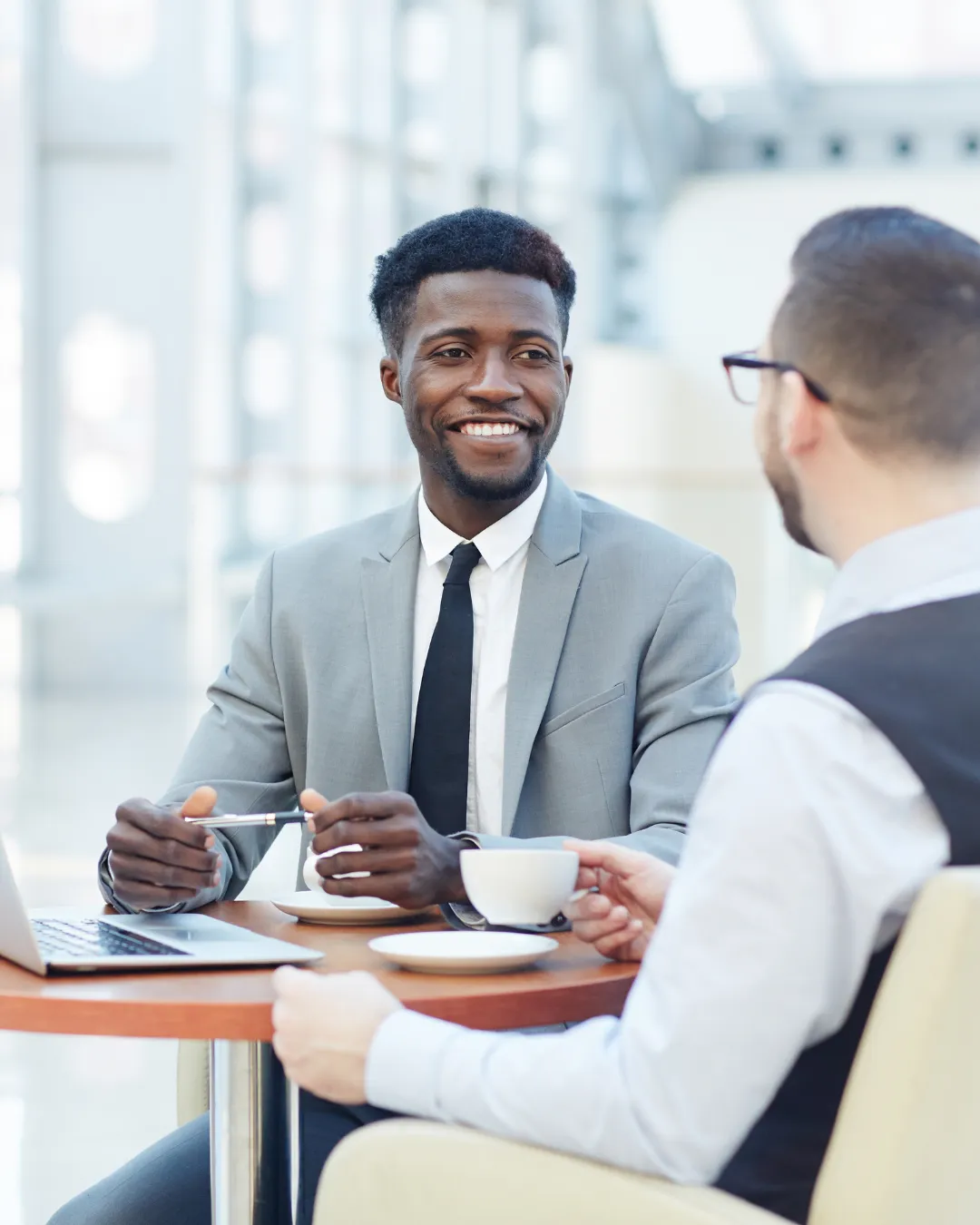 Modern, open-air room with floor-to-ceiling windows overlooking a calm ocean.   Wooden lounge chairs facing the water, with tall grasses near the edge.