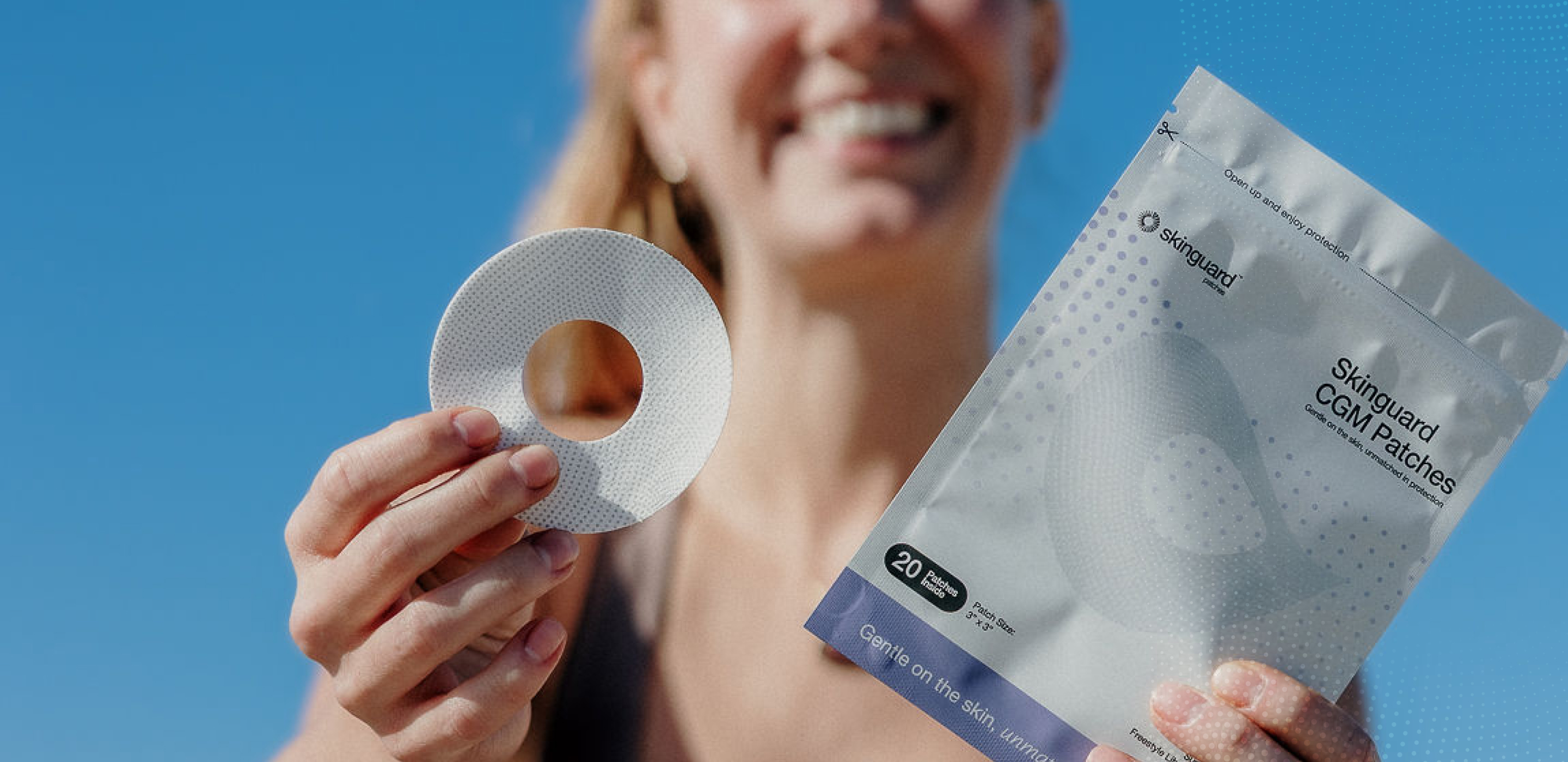 A person smiles while holding a CGM patch and its packaging against a clear blue sky.