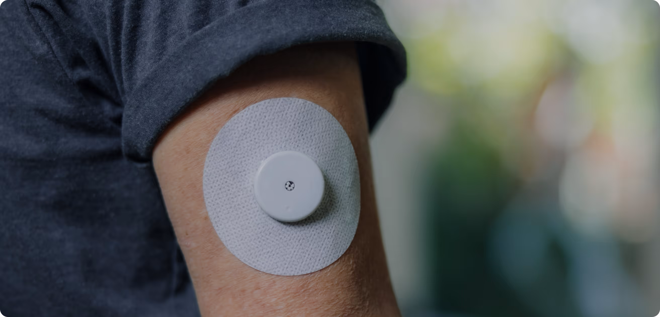 A person wearing a medical sensor patch on their upper arm.