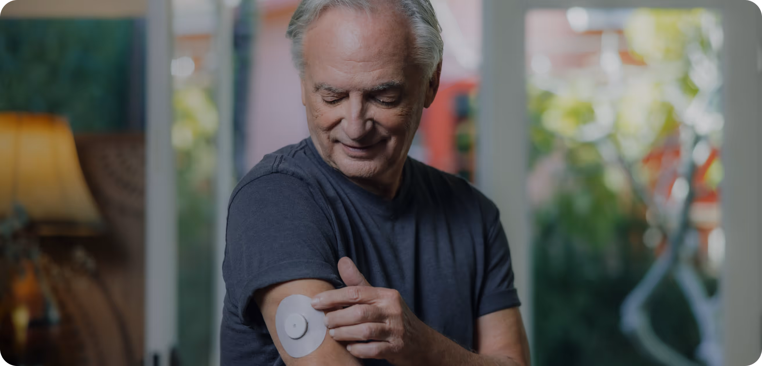 An older man applies a round medical patch to his upper arm.