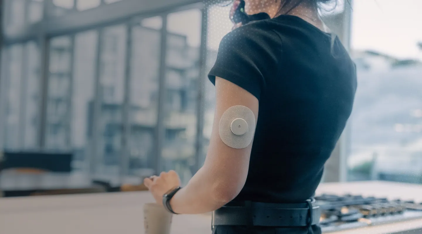 A person with a wearable sensor on their upper arm stands in a modern kitchen.