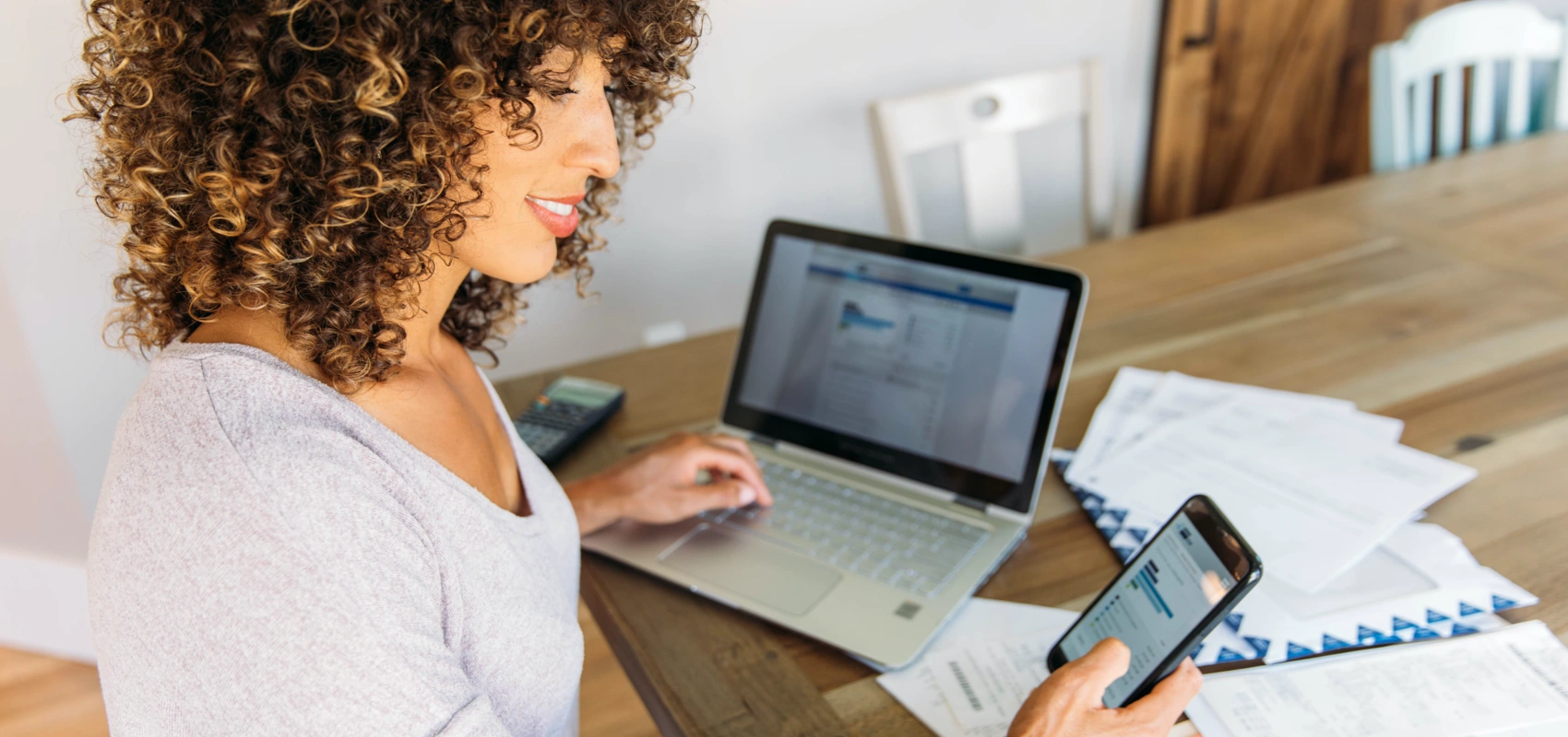 Woman looking at her phone and computer for charts of her money market account.