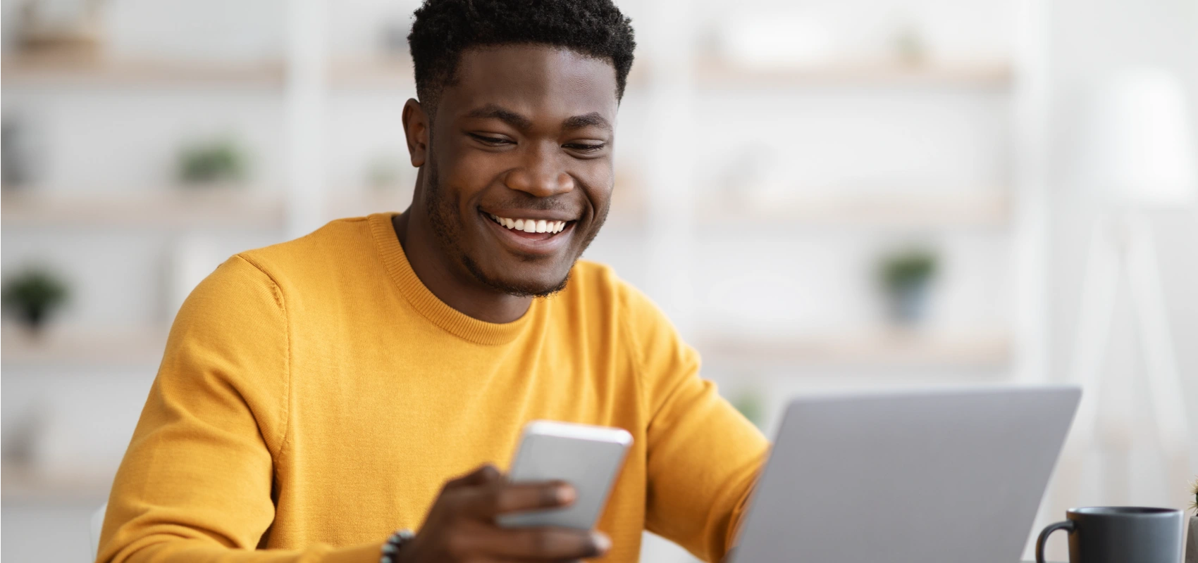 Man smiling while looking at his phone and laptop