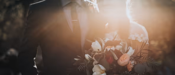 Man in suit holding a bouquet of flowers with sunlight shining behind.