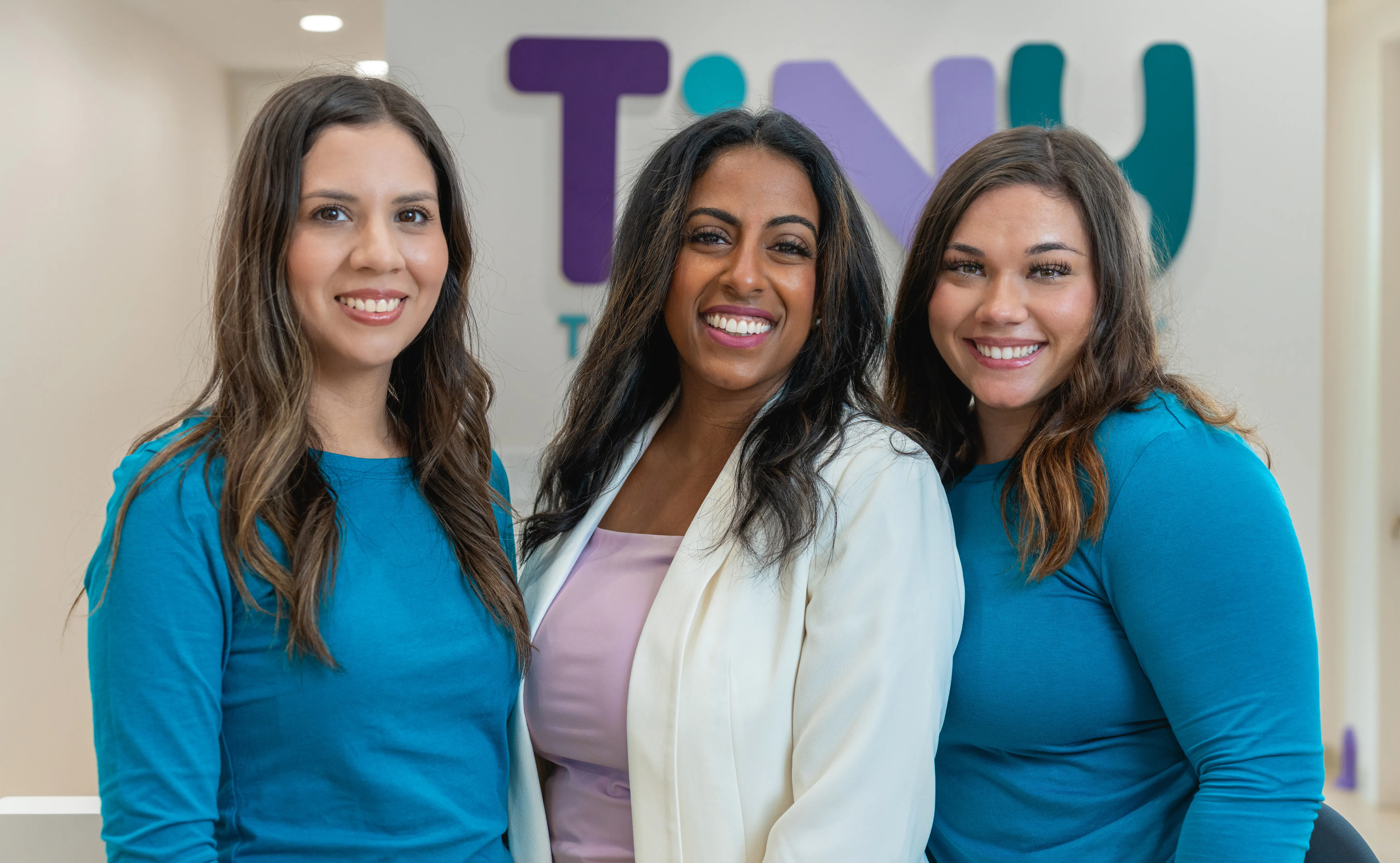 Dr. Sarah Arafat with two smiling team members at Tiny Tooth Company, standing in front of the clinic logo and showcasing a welcoming pediatric dental care environment.