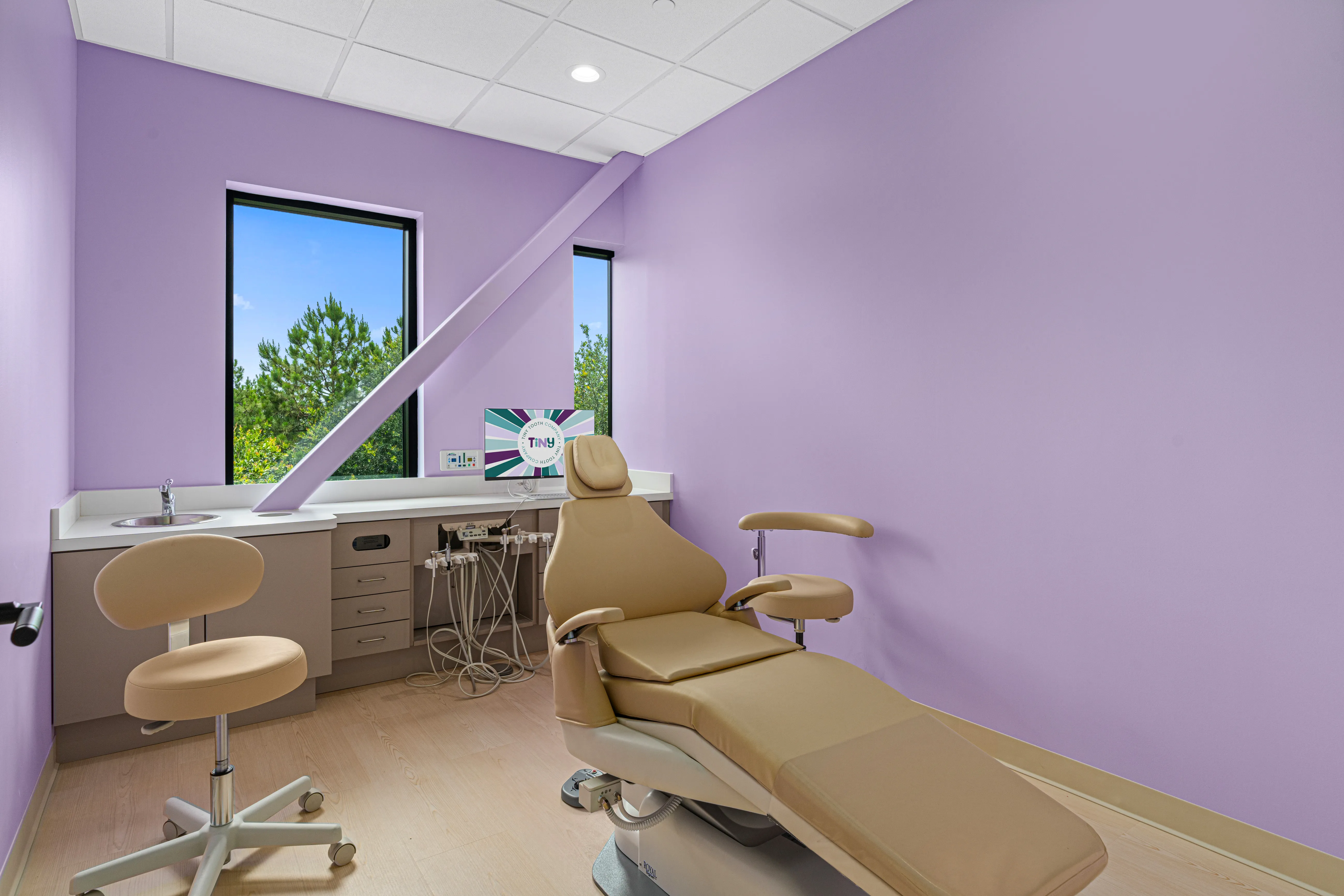 Private pediatric dental treatment room at Tiny Tooth Company, featuring soft lavender walls, natural light from large windows, and a tan dental chair with modern equipment.