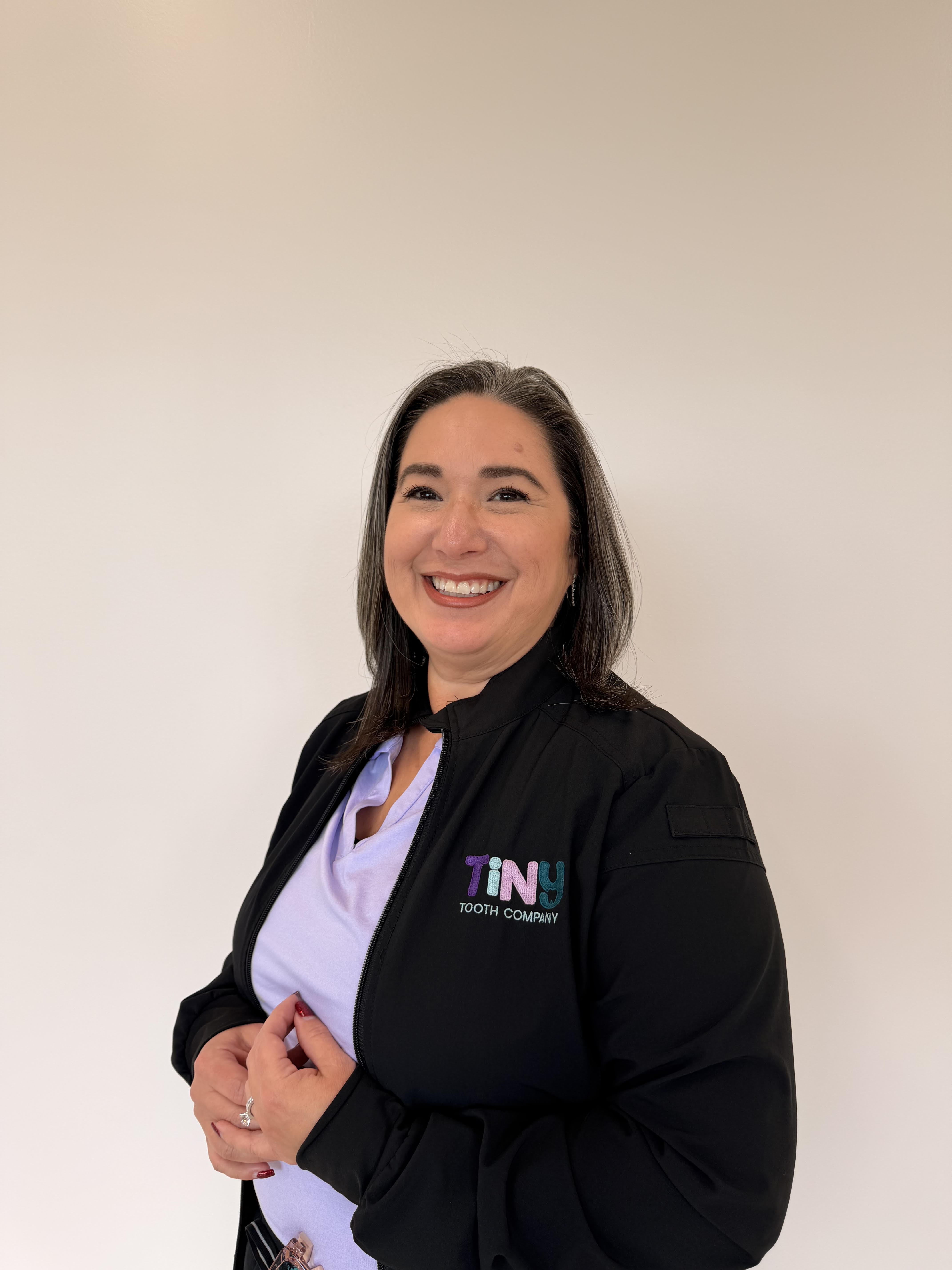 Patient Care Coordinator at Tiny Dental Company, smiling in a black Tiny Tooth Company jacket over a lavender scrub top
