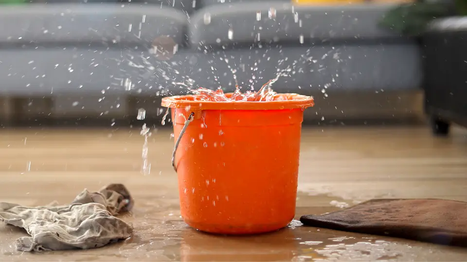 Fuite d'eau importante avec sol mouillé, serviettes pour éponger, sceau orange