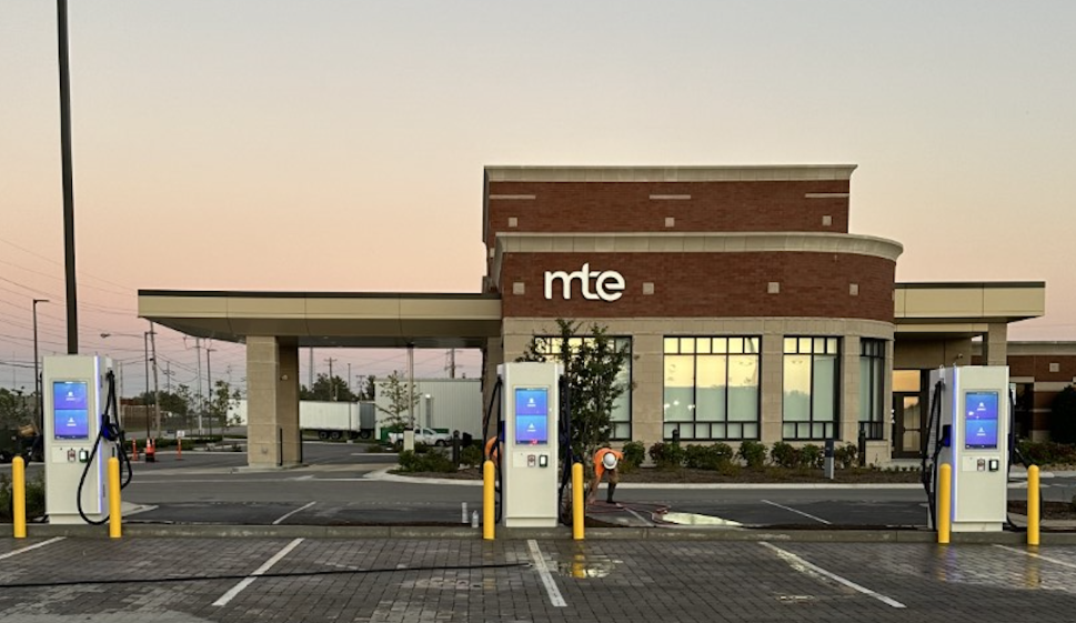 Three EV fast charging kiosks at a retail site at dusk
