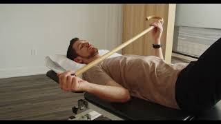 Physio démontrant mobilité en rotation externe de l'épaule sur le dos avec bâton