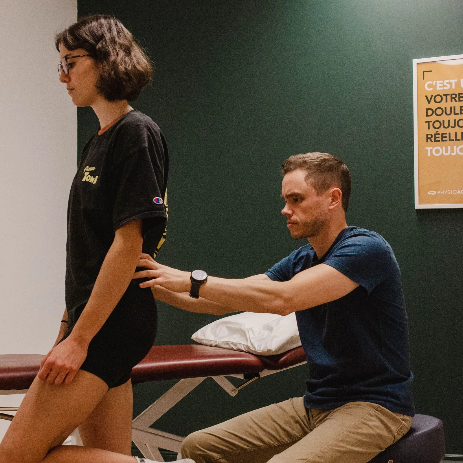 Physiothérapeute Physioactif évaluant la hanche, le bassin et la cuisse d'une patiente debout en physiothérapie
