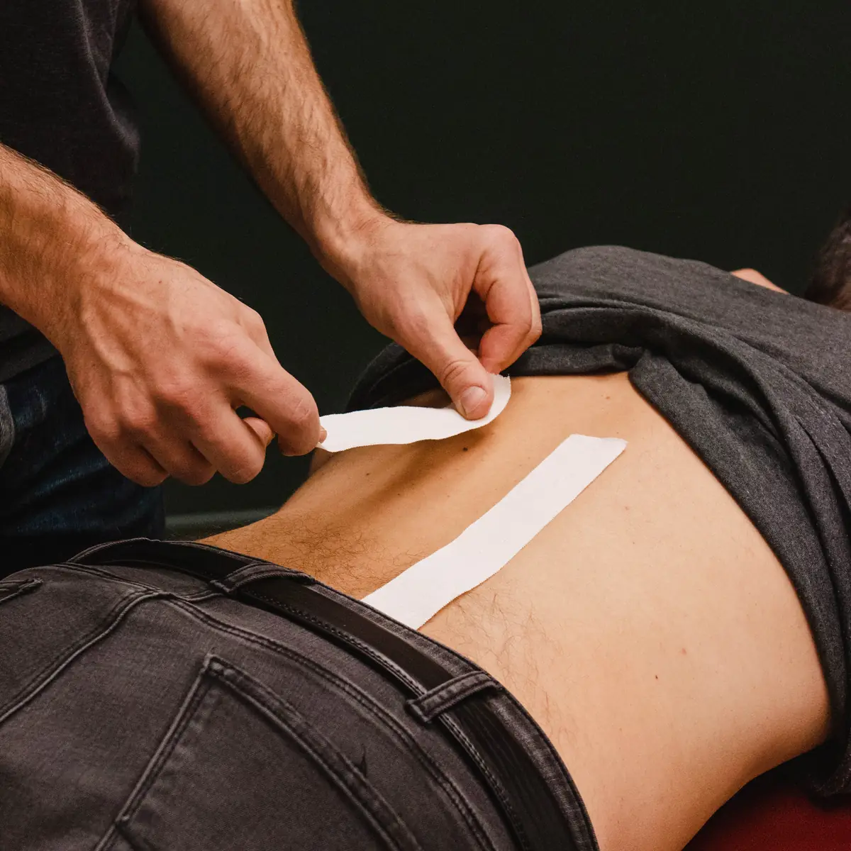 Physiothérapeute Physioactif appliquant des bandes de taping sur le bas du dos d'un patient en physiothérapie