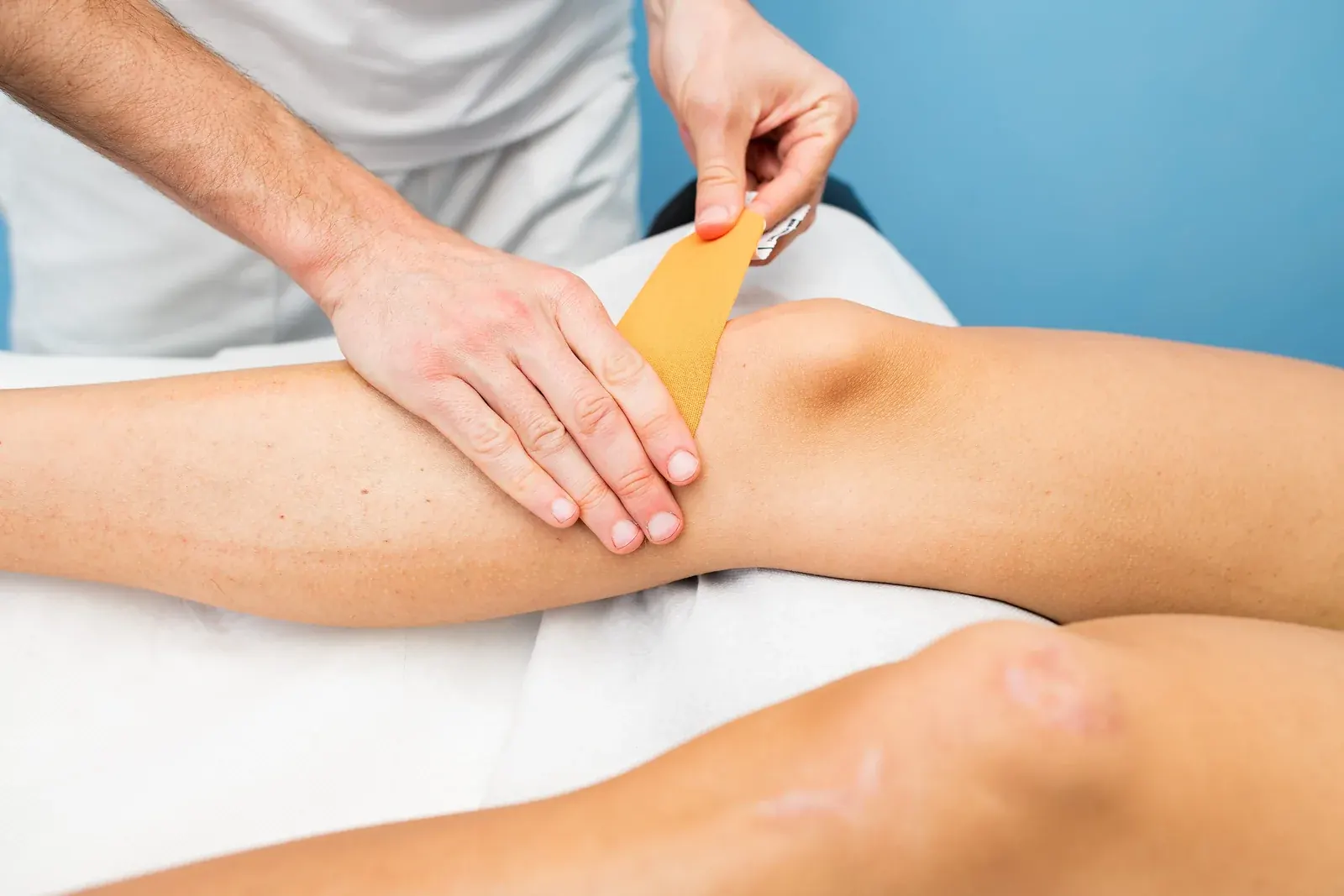 Pose de ruban de taping orange sur le genou en physiothérapie chez Physioactif