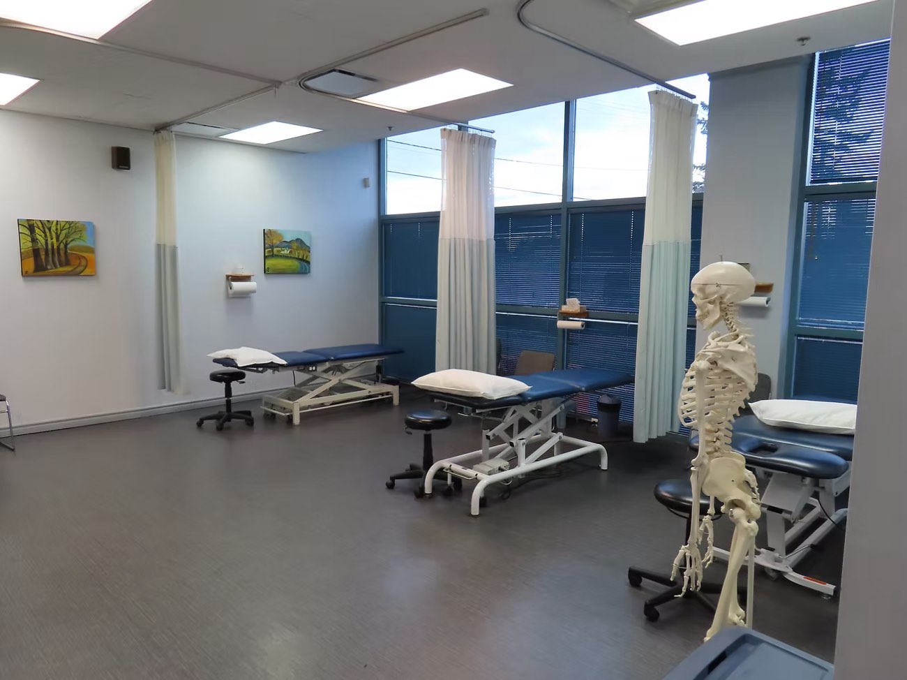 Salle de traitement de la clinique Physioactif Boucherville, tables de physiothérapie et squelette anatomique devant de grandes fenêtres