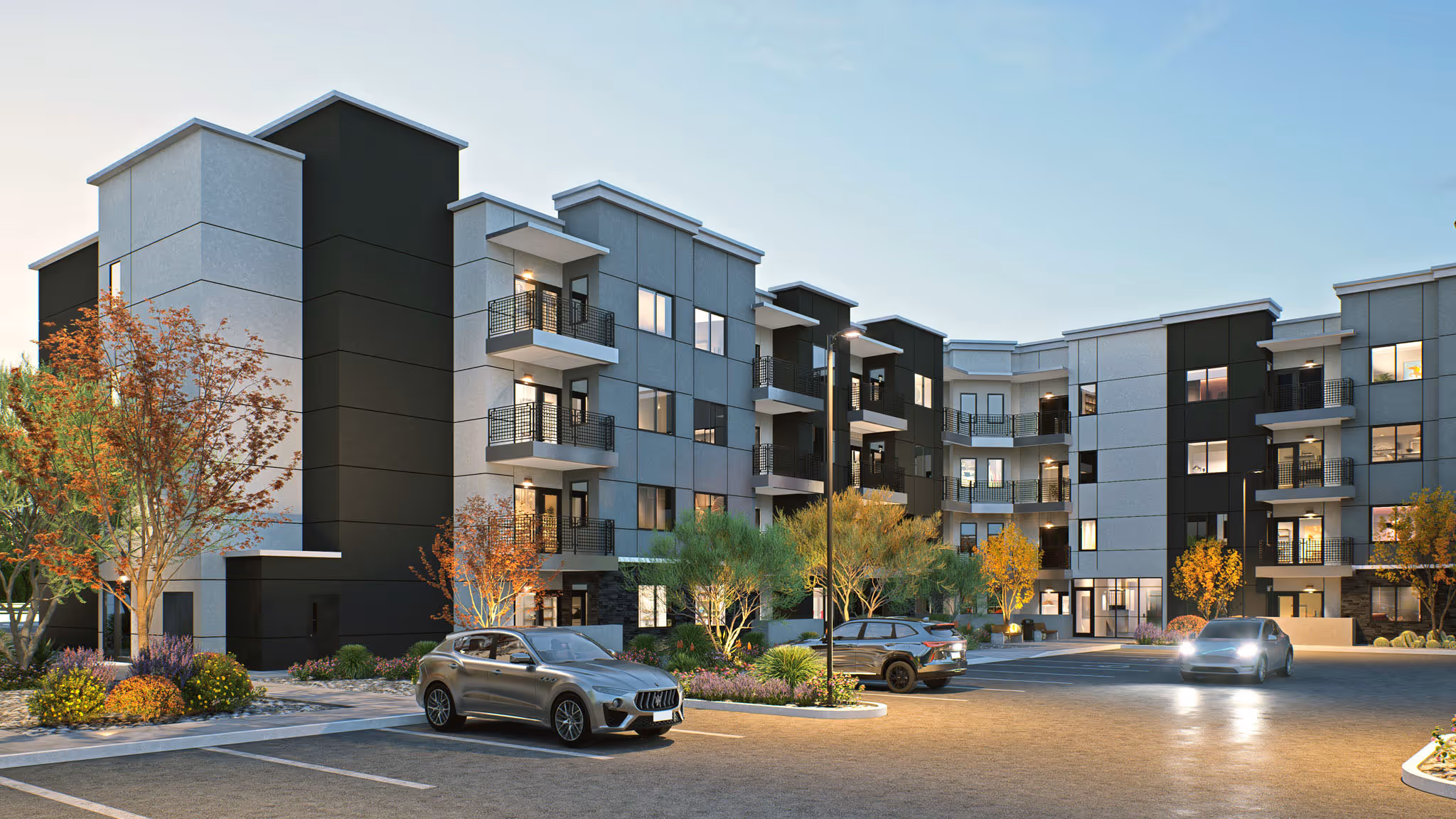 Exterior night rendering of a modern apartment building with balconies and desert landscaping, showing cars parked in a well-lit lot at Avondale Commons in Avondale, AZ.