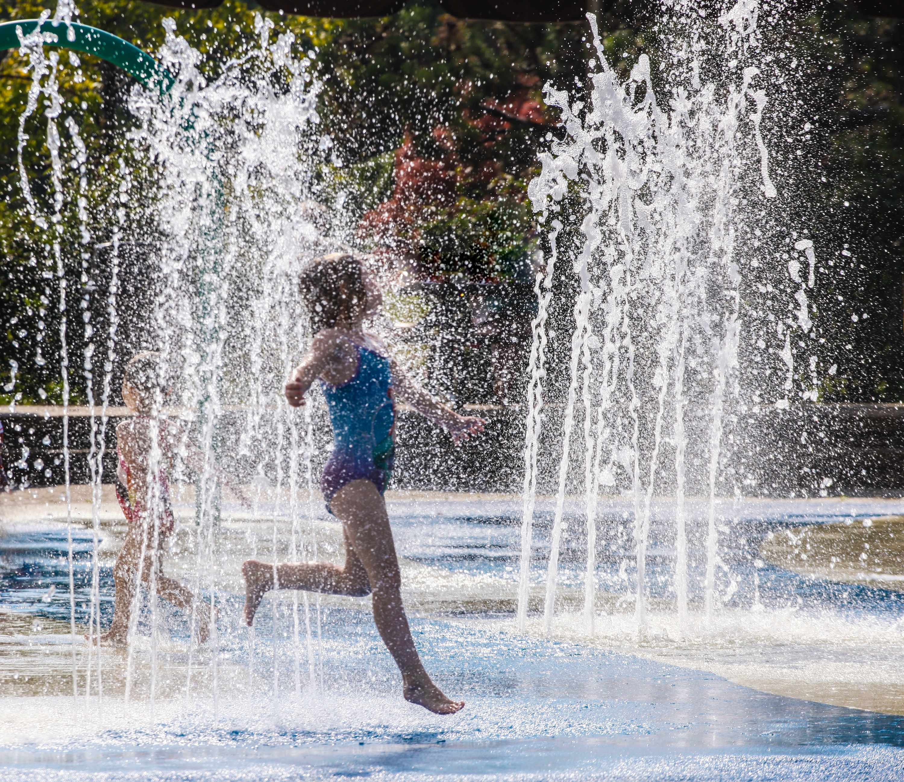 Child joyfully playing in a splash pad with water jets, depicting a fun outdoor amenity or local recreation option near Avondale Commons in Avondale, AZ