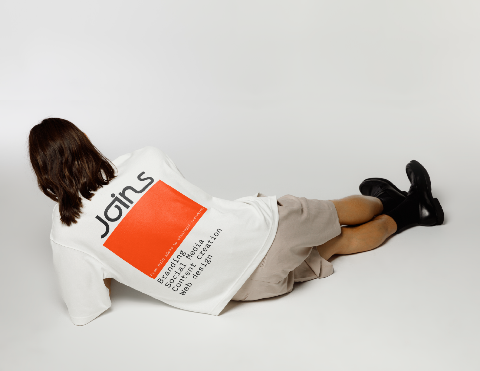 Woman lying on her back wearing a white Joins shirt