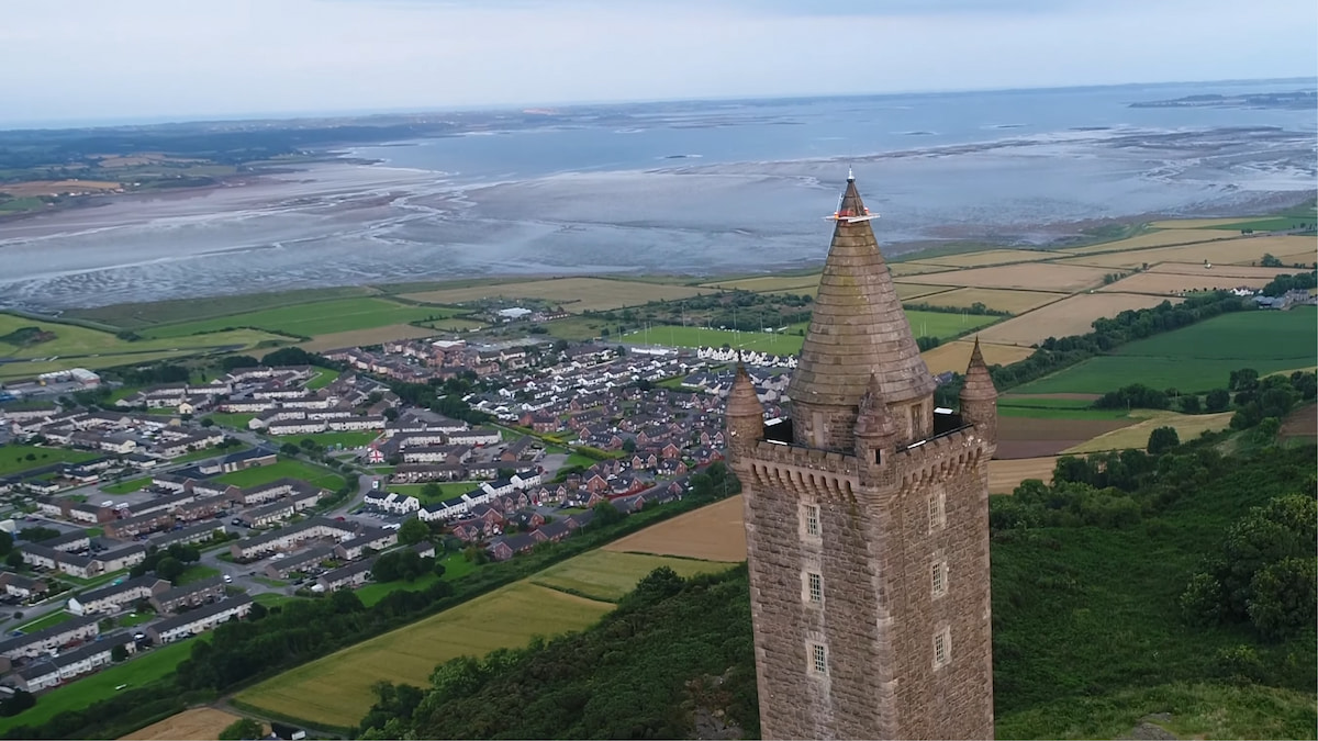 View over Newtownards, with Scrabo Tower prominently in the foreground, residential neighborhoods spreading out below, and Strangford Lough visible in the background.