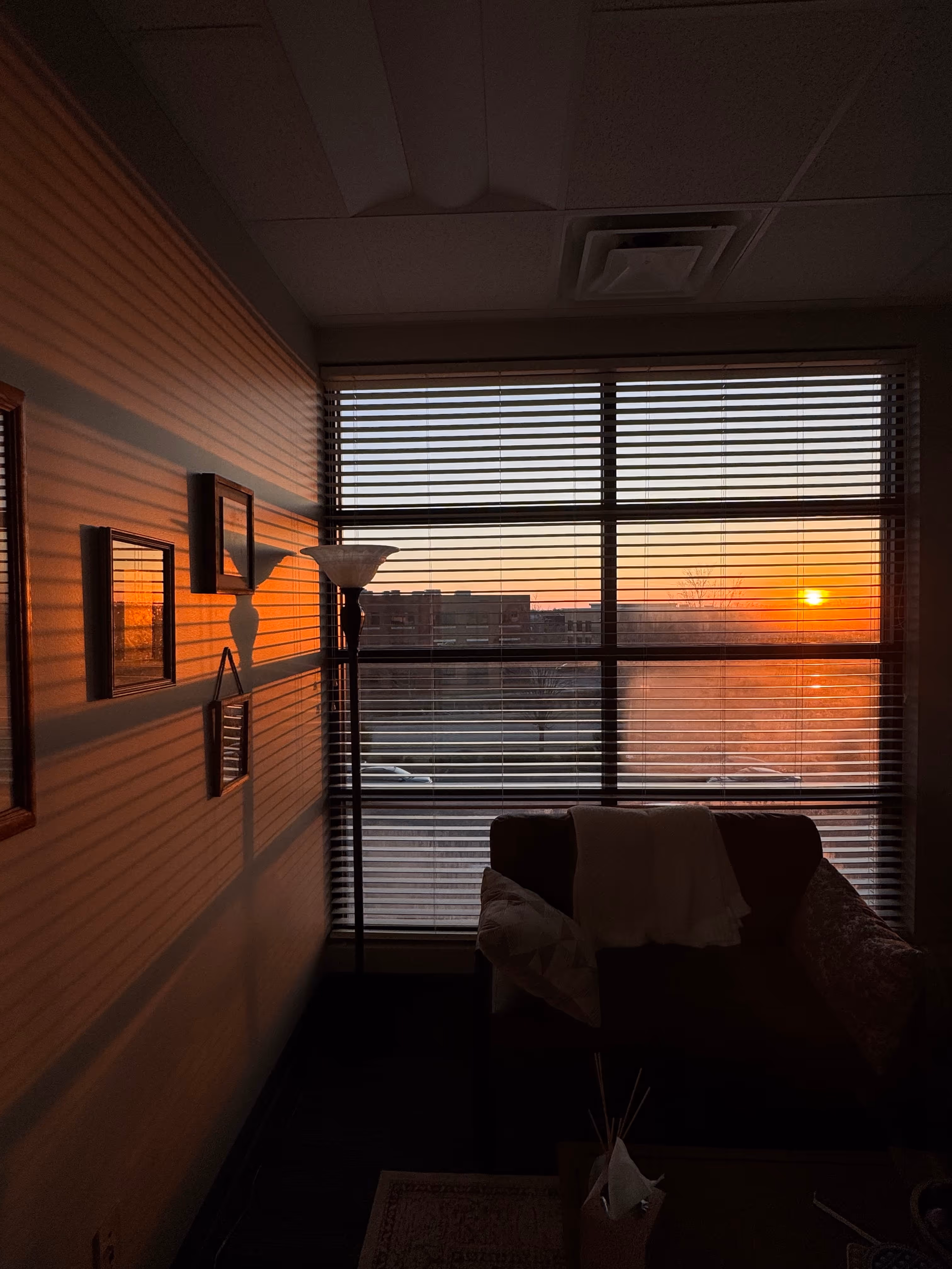 Sunset light casts striped shadows from blinds on a wall in the therapy room in Lexington, KY with a couch and lamp.