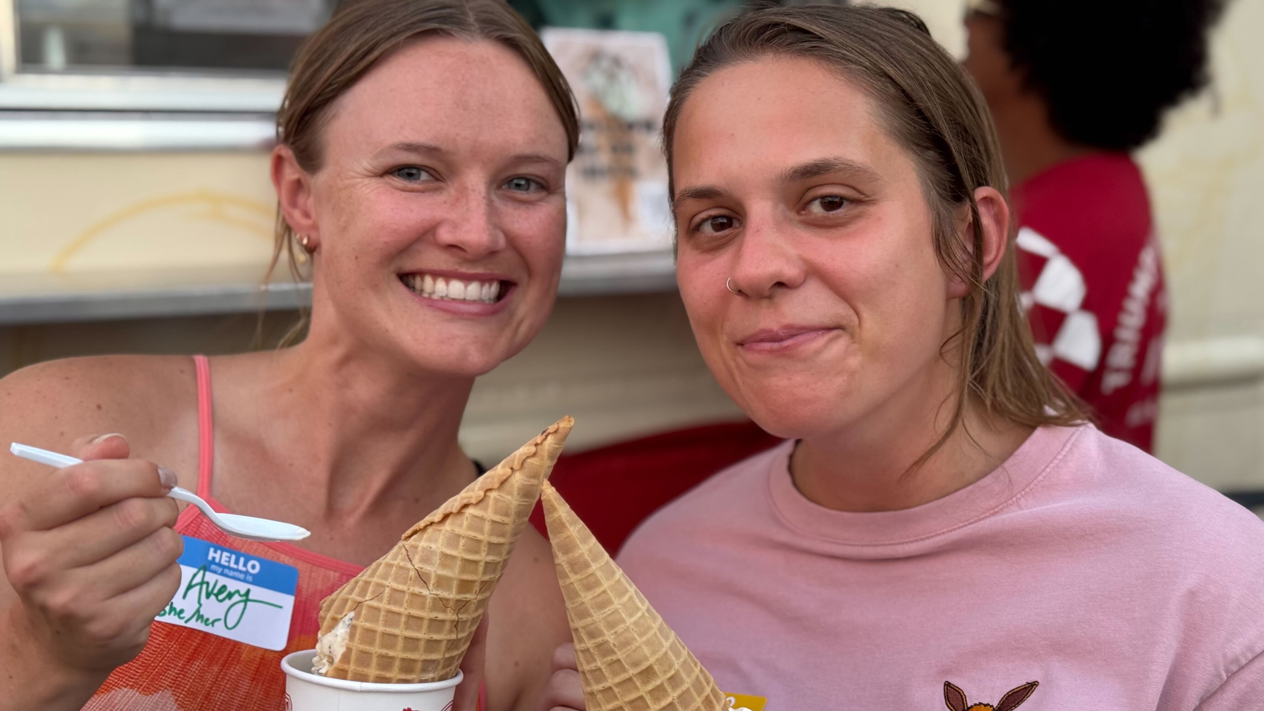 Two people smiling, holding waffle cones with ice cream.