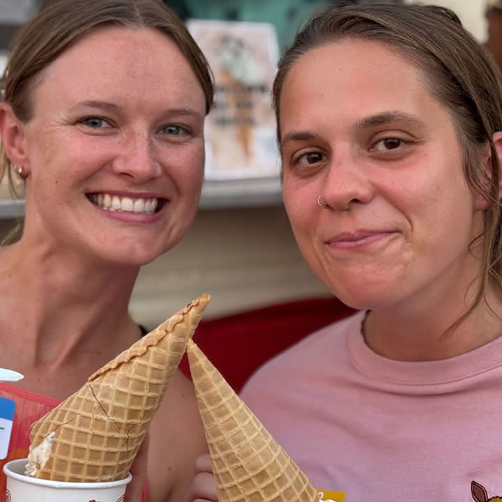 Two people smiling, holding waffle cones with ice cream.
