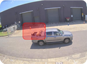 Silver pickup truck parked on a road beside an industrial building with three large loading bay doors.