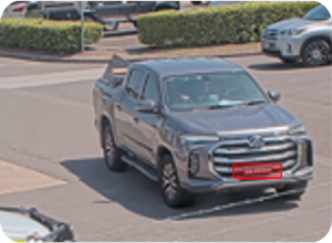 Gray pickup truck driving on a street with other cars and bushes in the background.