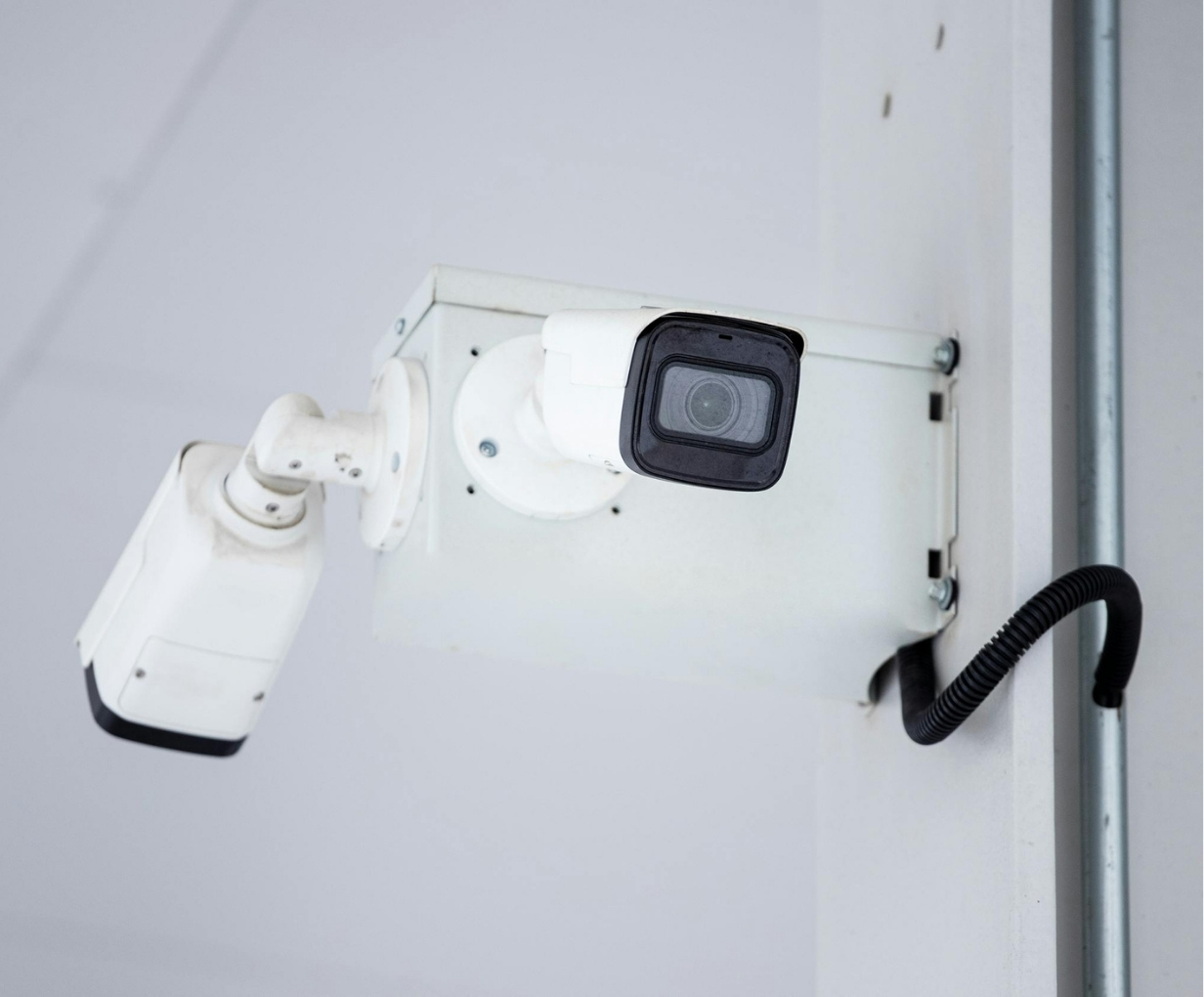 White security camera mounted on a wall with a coiled black cable connected.