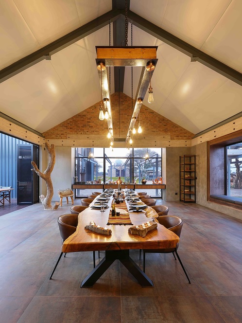 Modern dining room with a long, natural wood table set with plates and bowls, surrounded by brown leather chairs under industrial-style pendant lights.