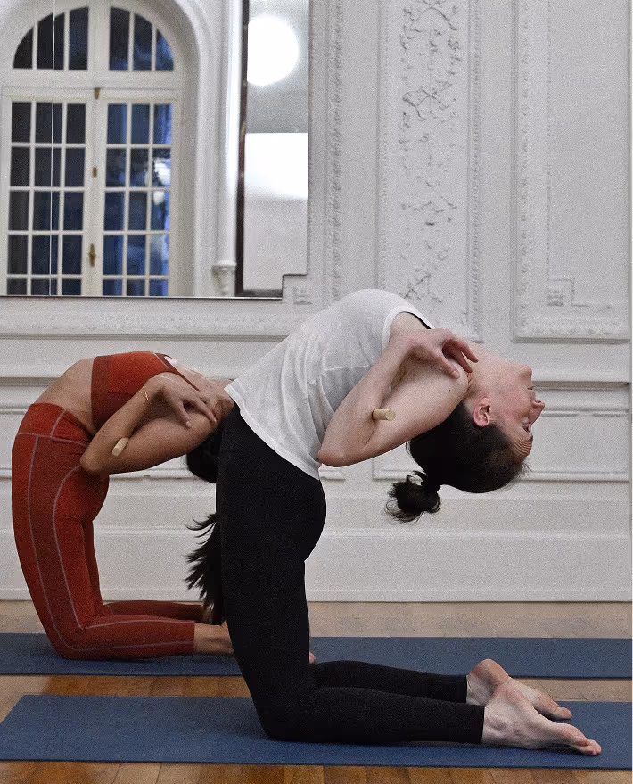 Deux pratiquantes de yoga qui exécutent la posture du chameau (ustrasana) avec un bâton dans le dos