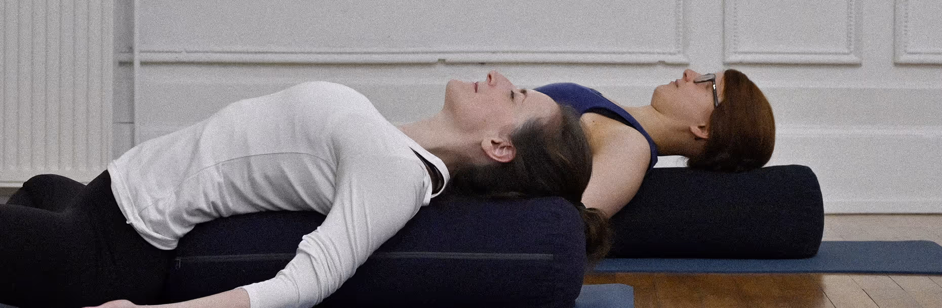Deux filles en supta baddhakonasana (papillon couché) sur un coussin.