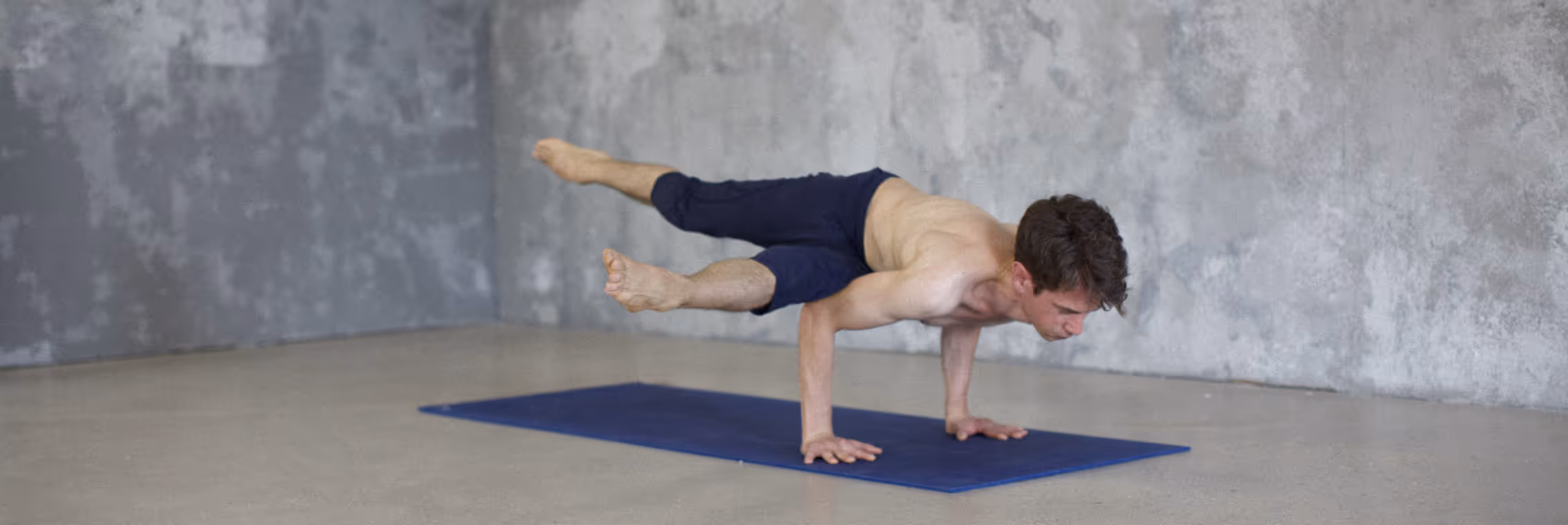 Antoine dans kaundyanasana, posture d'équilibre sur les mains, devant un mur gris