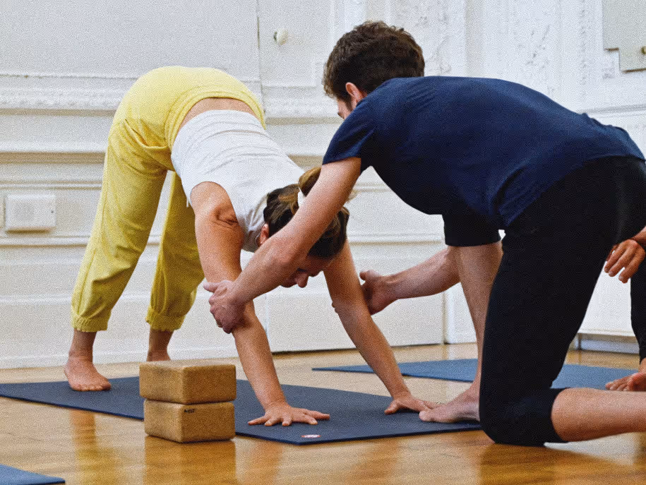 Antoine ajustant une élève en adhomukha svanasana, posture du chien la tête en bas