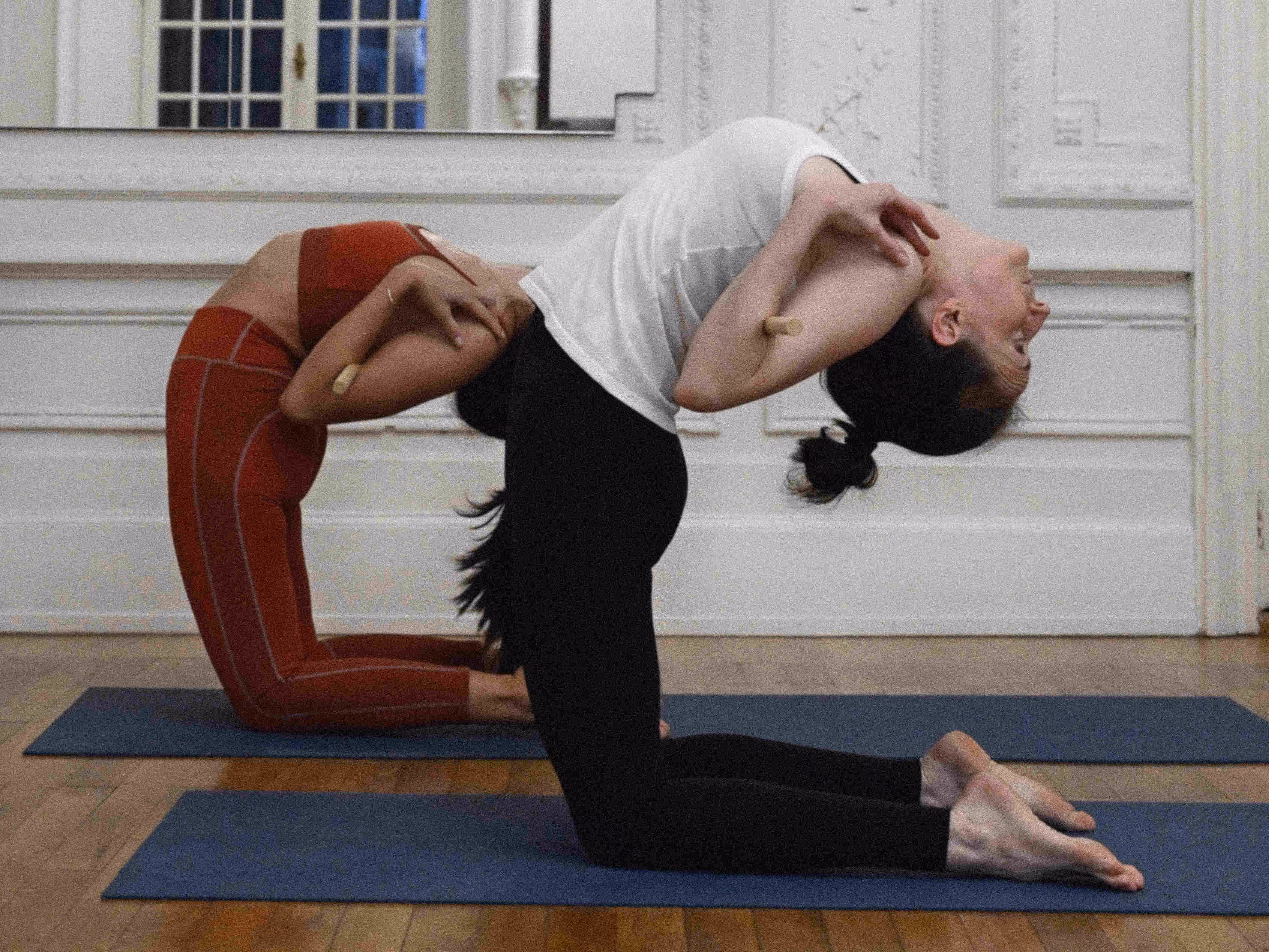 Deux pratiquantes de yoga en ustrasana, posture du chameau, avec un baton dans le dos