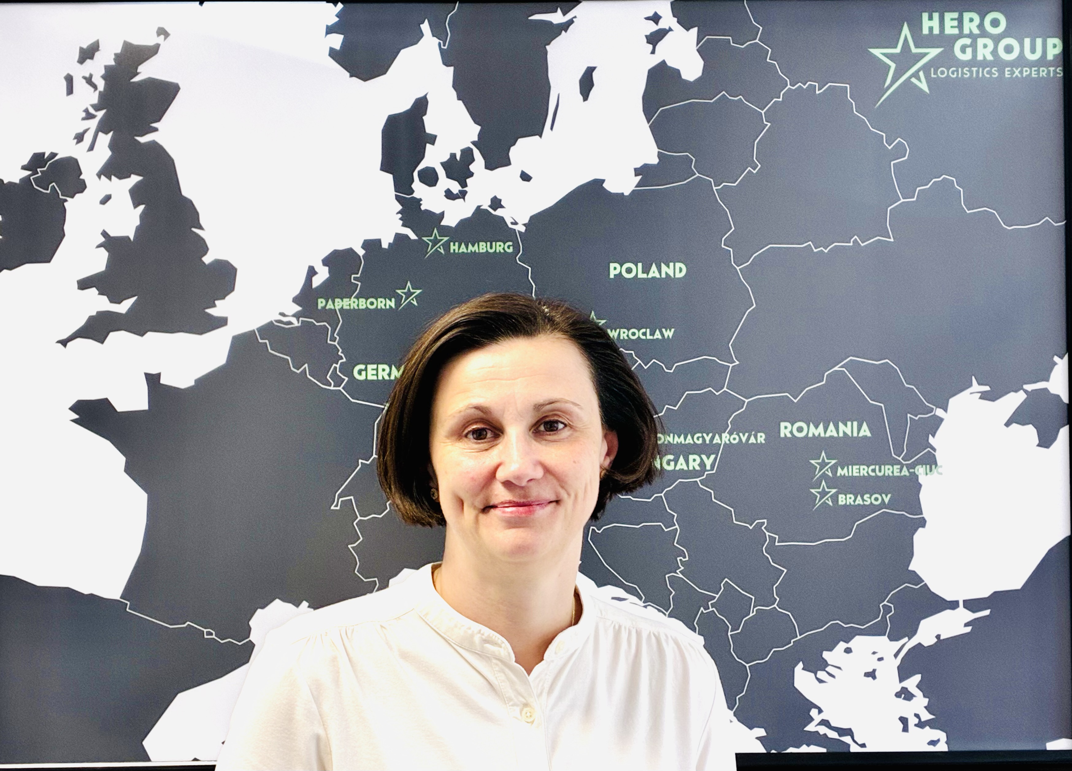 Frau vor einer Landkarte von Europa mit hervorgehobenen Städten und dem Logo von Hero Group oben rechts.