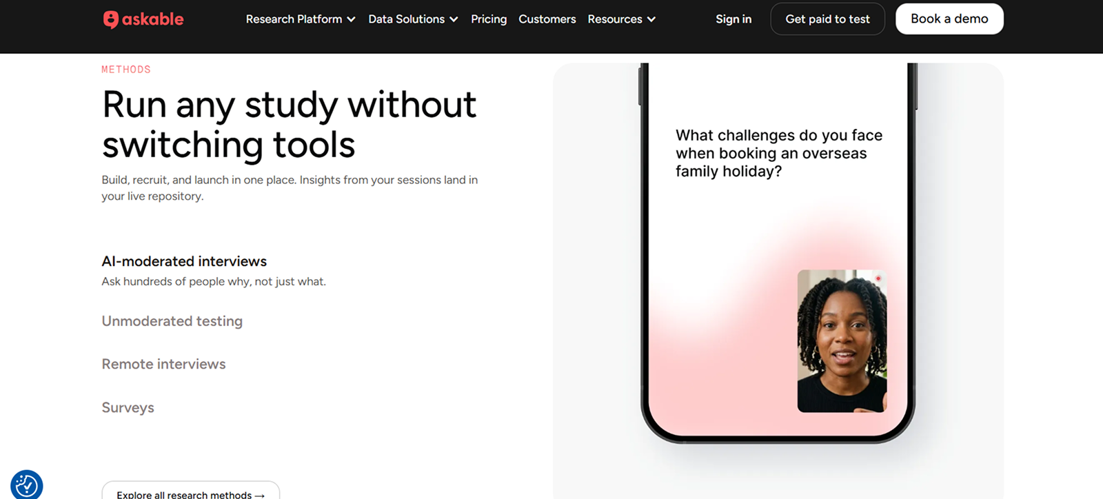 Webpage section from Askable showing research methods with the headline 'Run any study without switching tools' and a smartphone screen displaying a woman speaking with the question 'What challenges do you face when booking an overseas family holiday?'