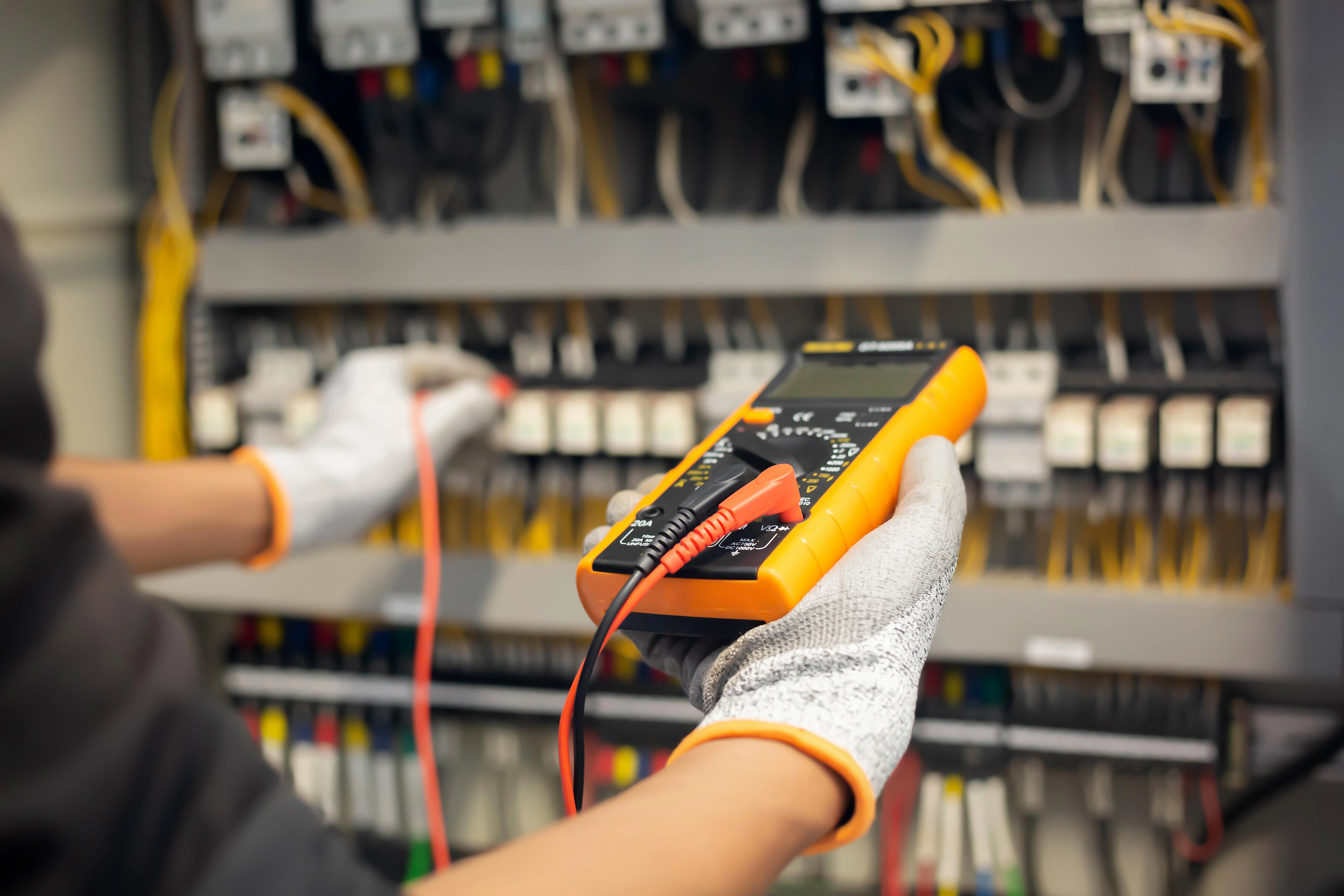 A person wearing gloves uses a multimeter to check an electrical panel. 
