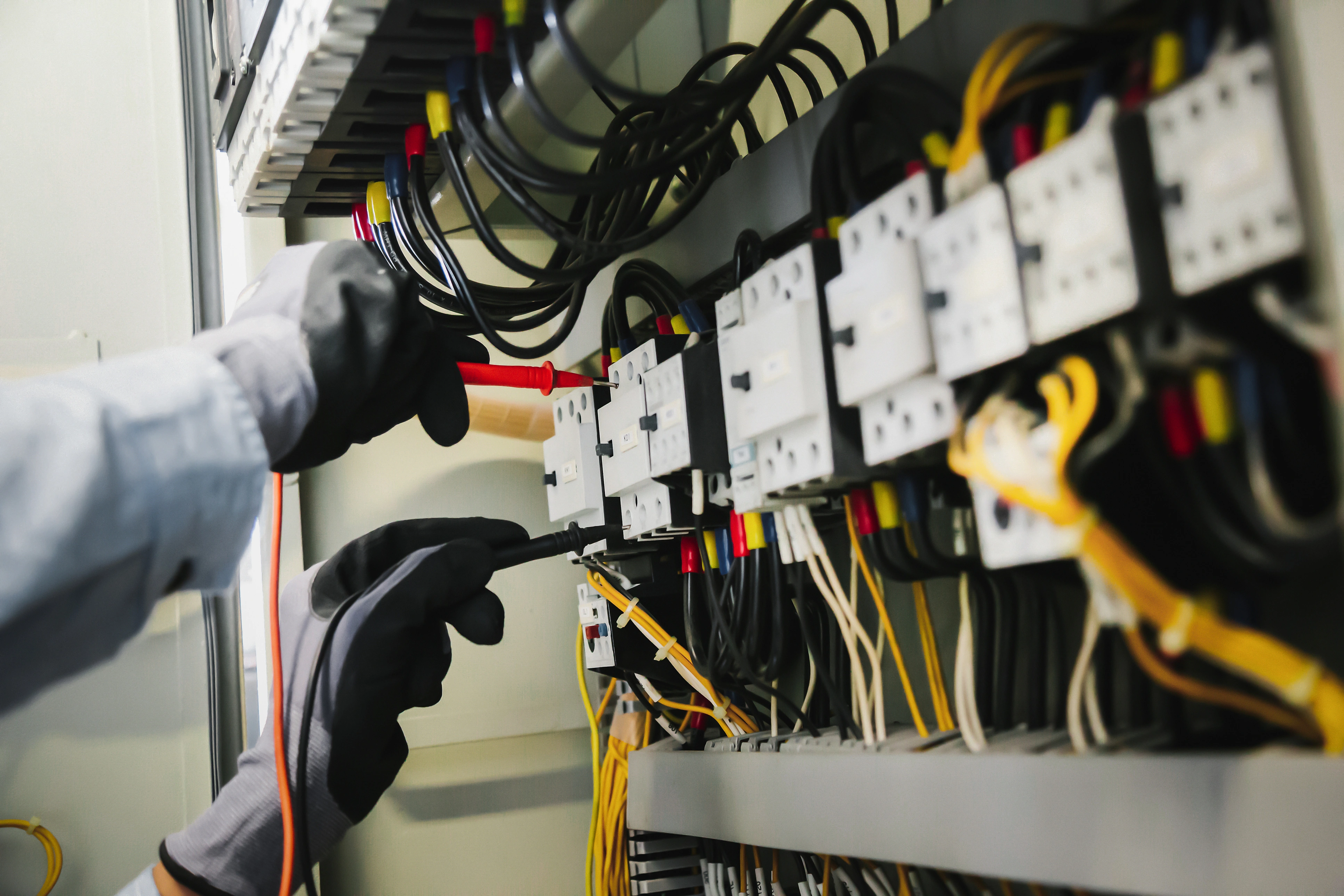 Hands wearing gloves use tools to work on a complex electrical panel.