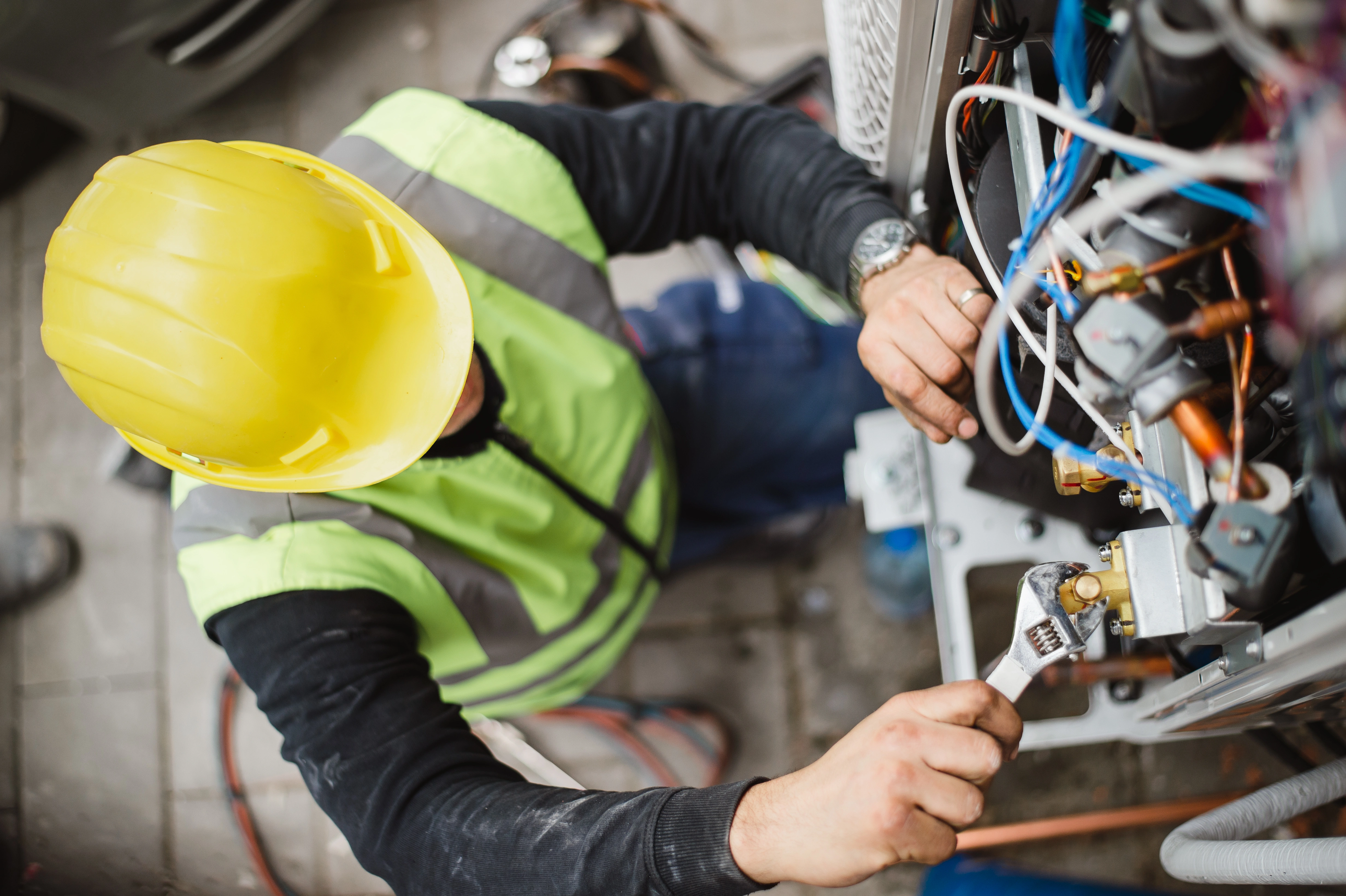 Worker in a yellow hard hat and green safety vest using a wrench on machinery. 