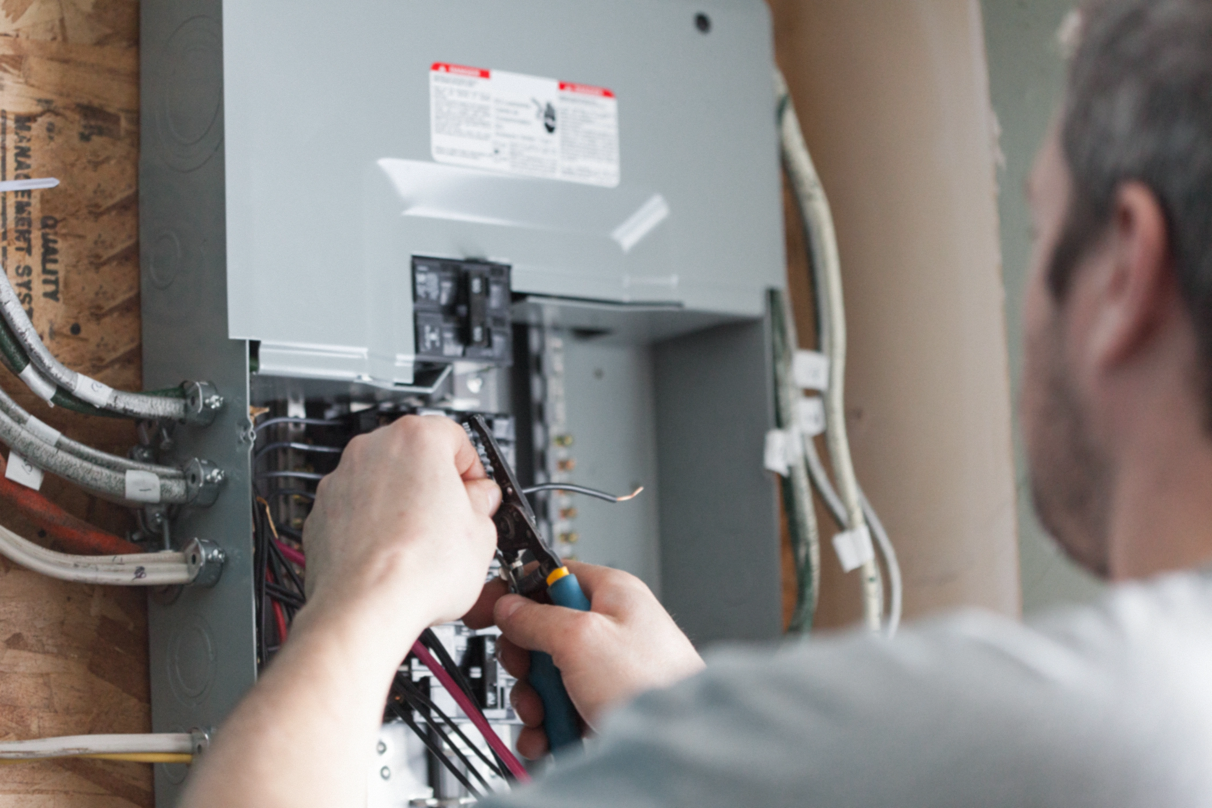 A person repairs an electrical panel, using pliers to adjust wiring.