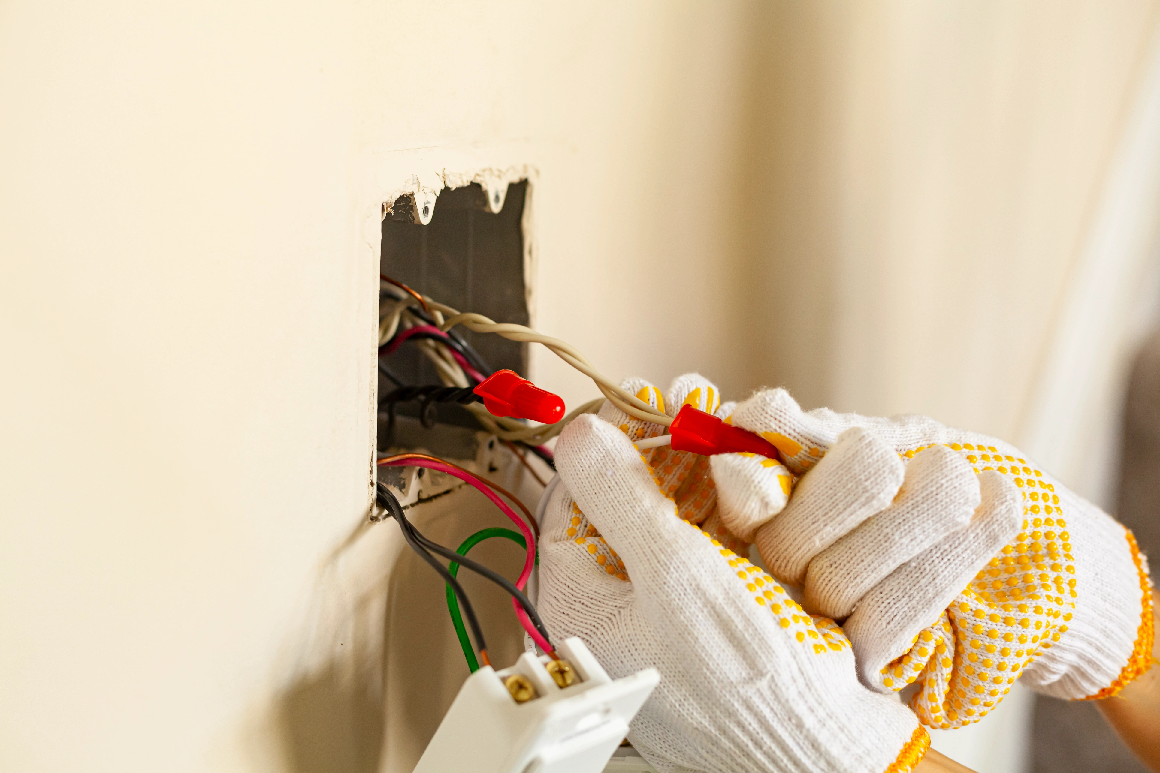 Electrician hands with white and yellow gloves repairing a wall socket.