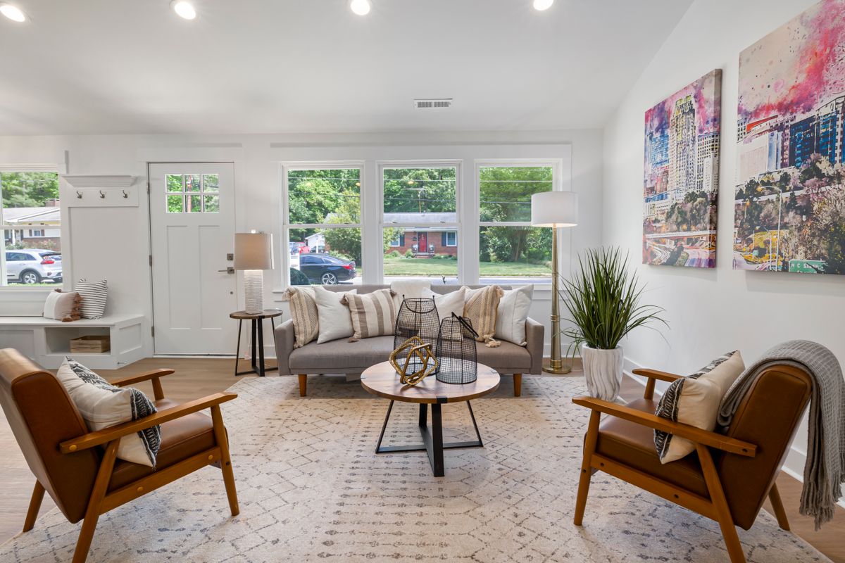 Bright living room with a grey sofa, two leather armchairs and large windows, photographed wide for a rental listing