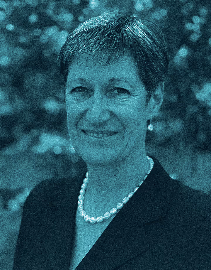 An image of a woman in a blazer, with short hair wearing a pearl necklace