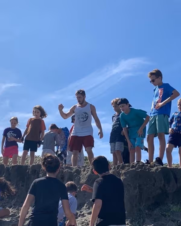 Group of children and a man standing on a rocky ledge under a clear blue sky.