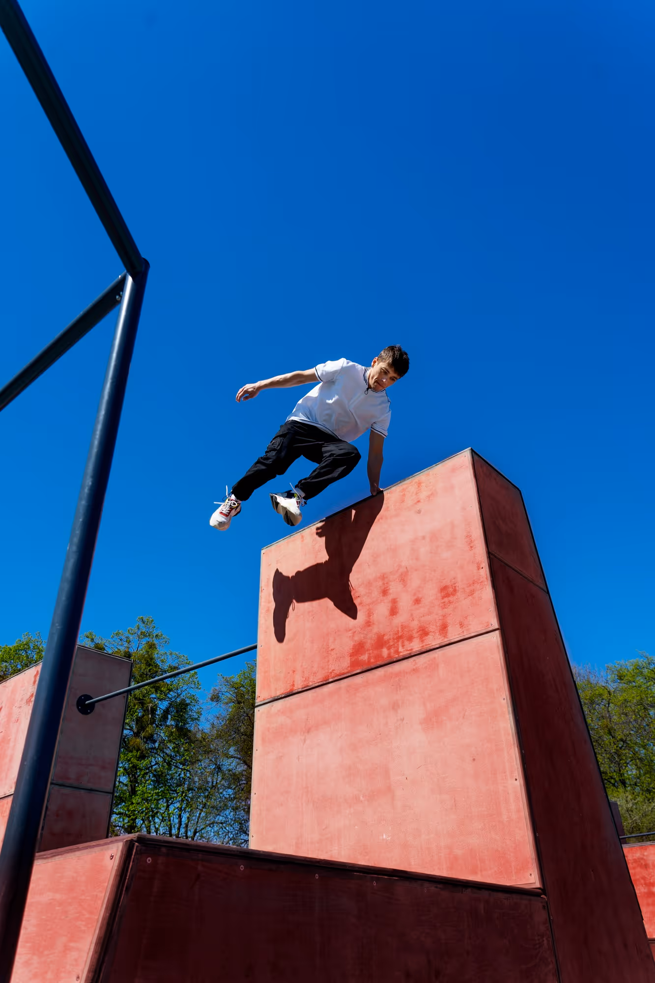 Young man performing a parkour jump off a tall red concrete structure against a clear blue sky.