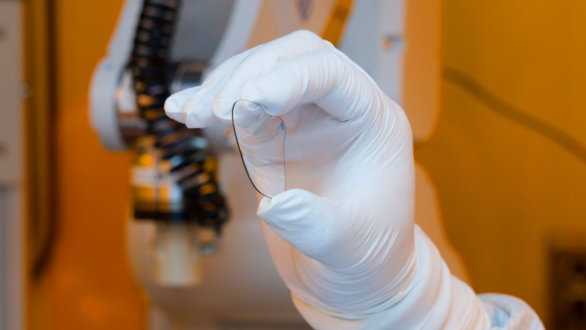 A gloved hand holds a waveguide, with lab machinery in the background.