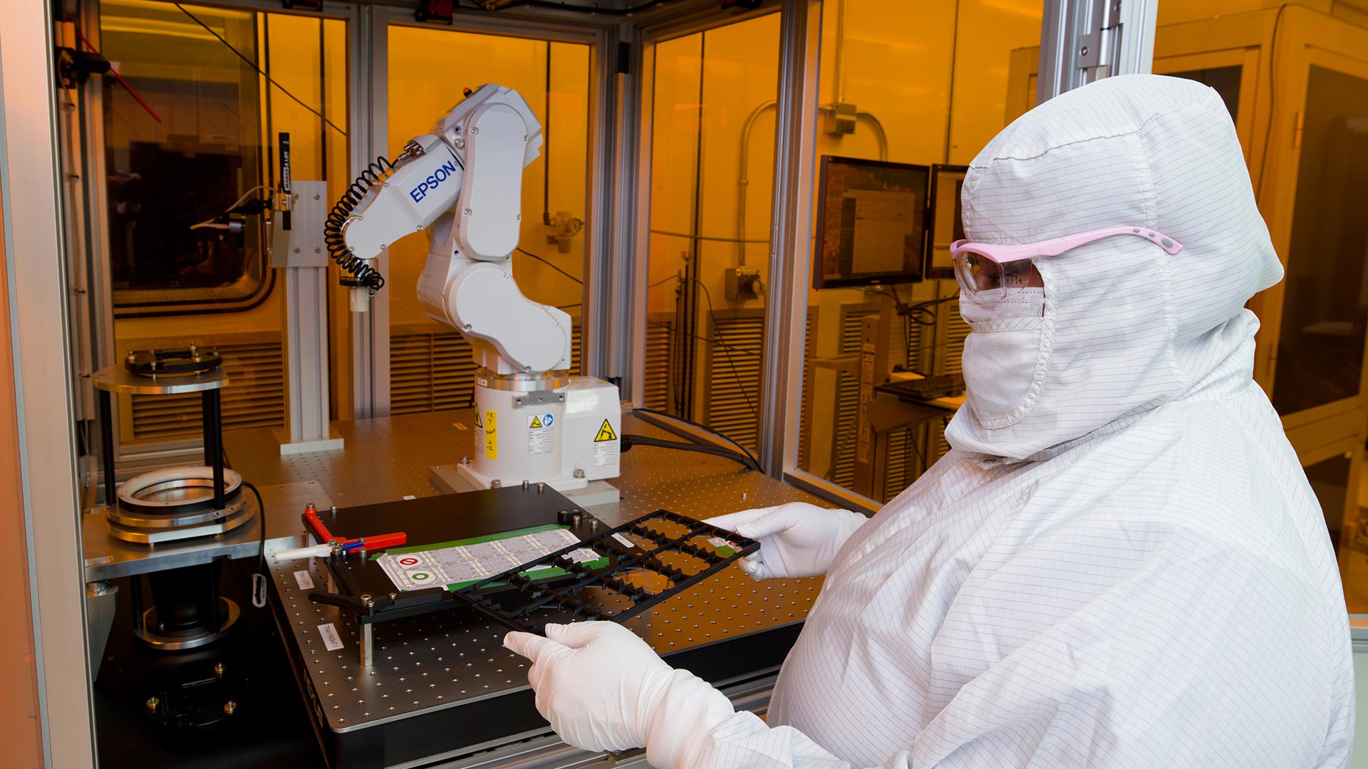 An engineer in lab gear holds a waveguide mold in front of an inspection machine.
