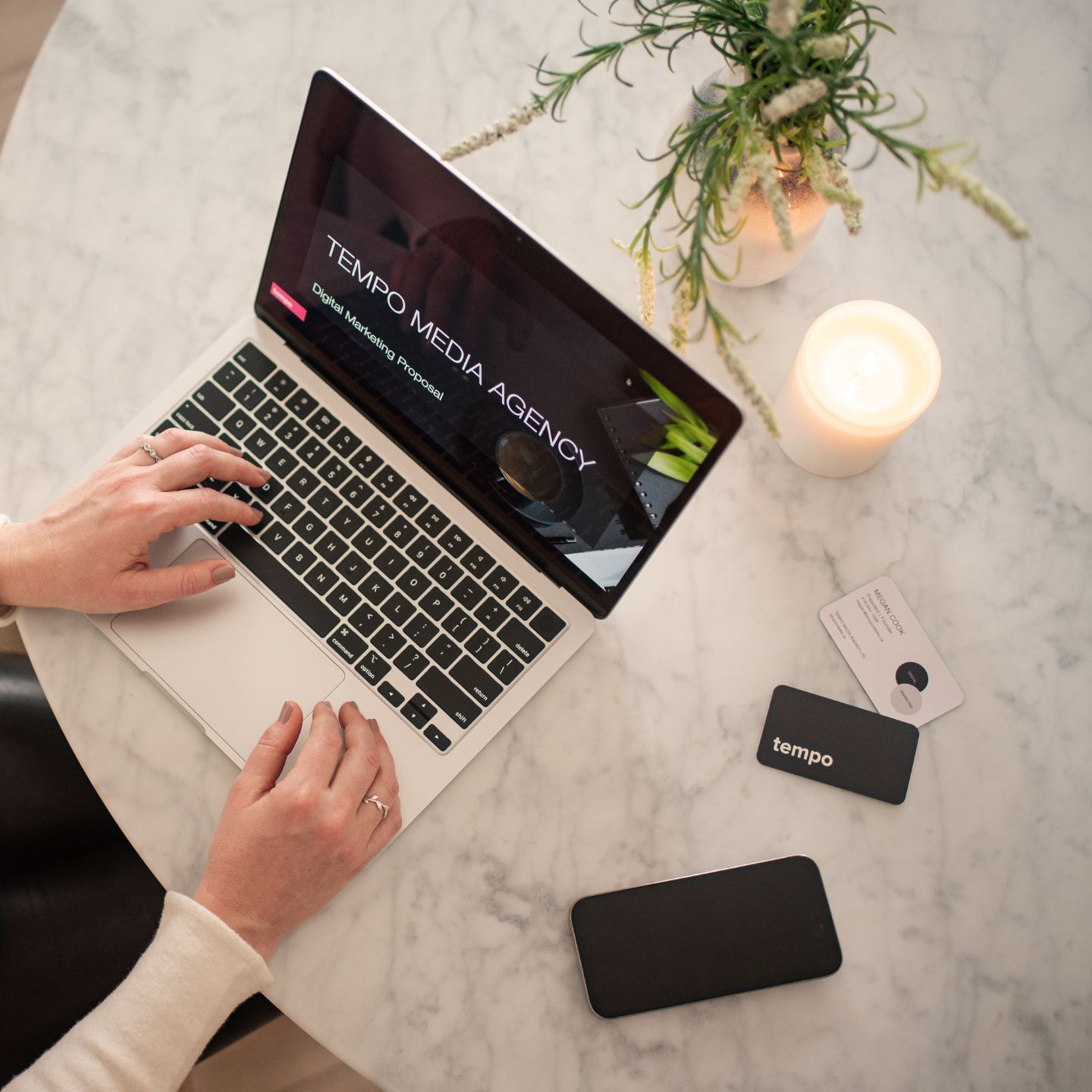 laptop open with a digital marketing proposal by Tempo Media Agency on it. The laptop is on a white marble table with an iPhone and business cards. 