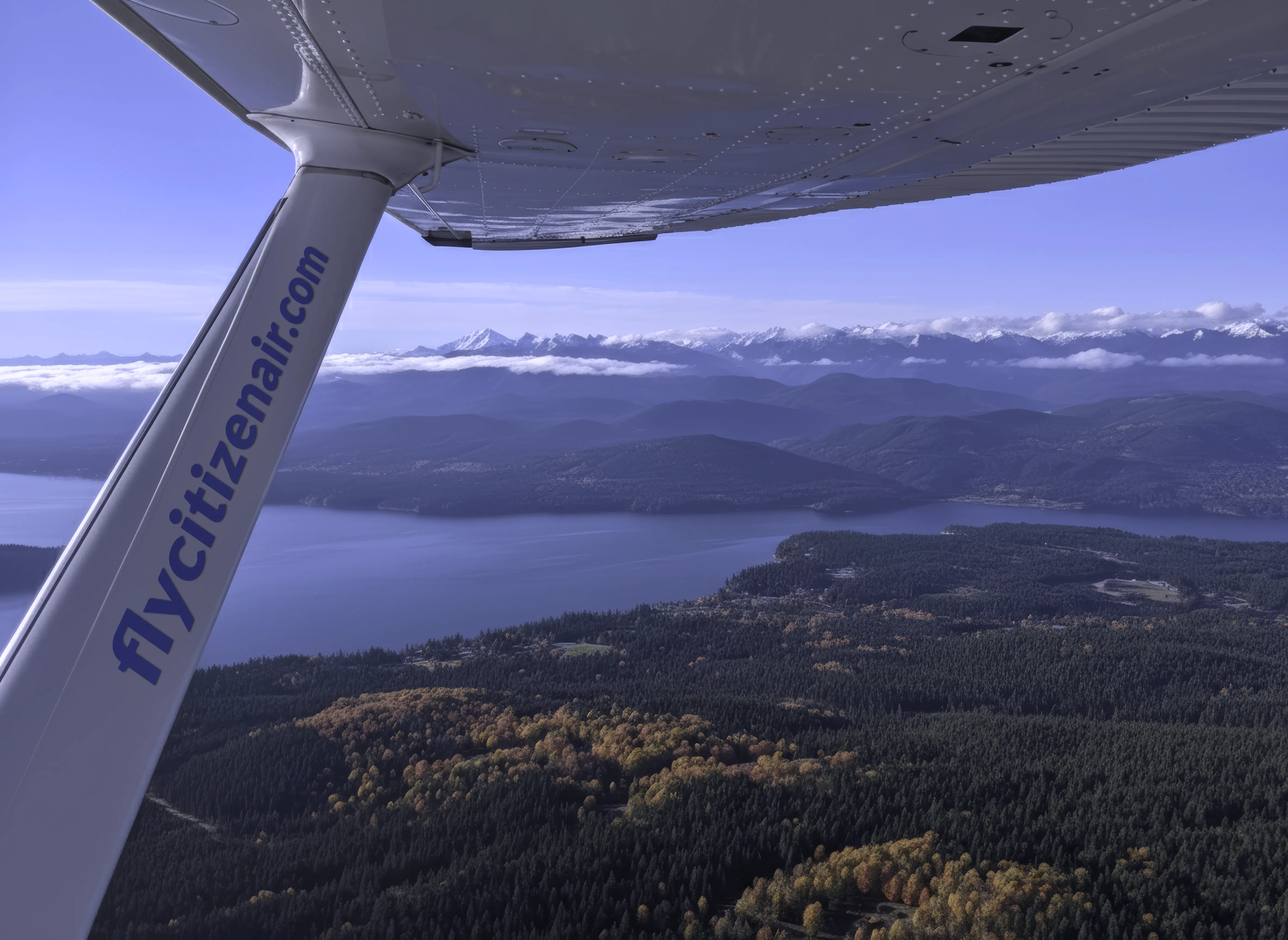 View over Puget Sound from a Cessna aircraft. The wing strut is visible, showing the url flycitizenair.com