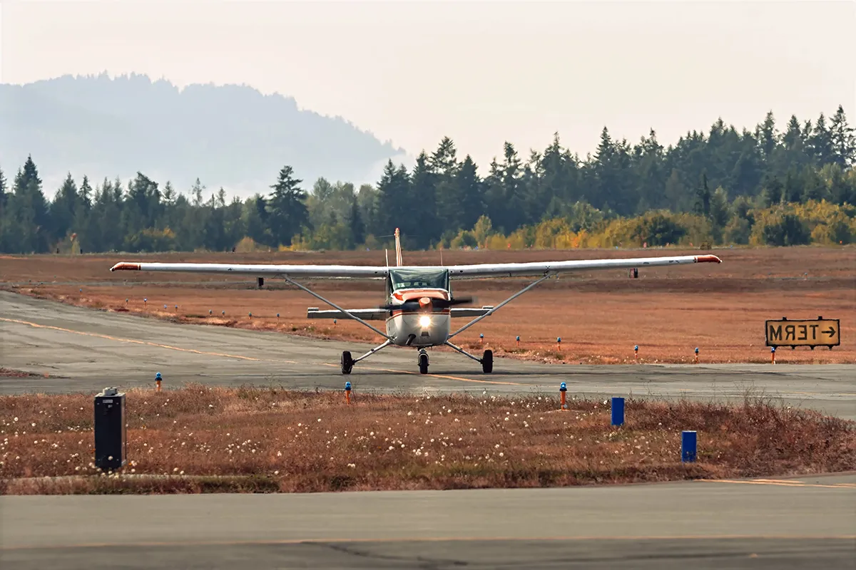 Cessna 172 taxing on the runway at Williams Fairchild International Airport in Port Angeles, with evergreens and mountains in the distance.